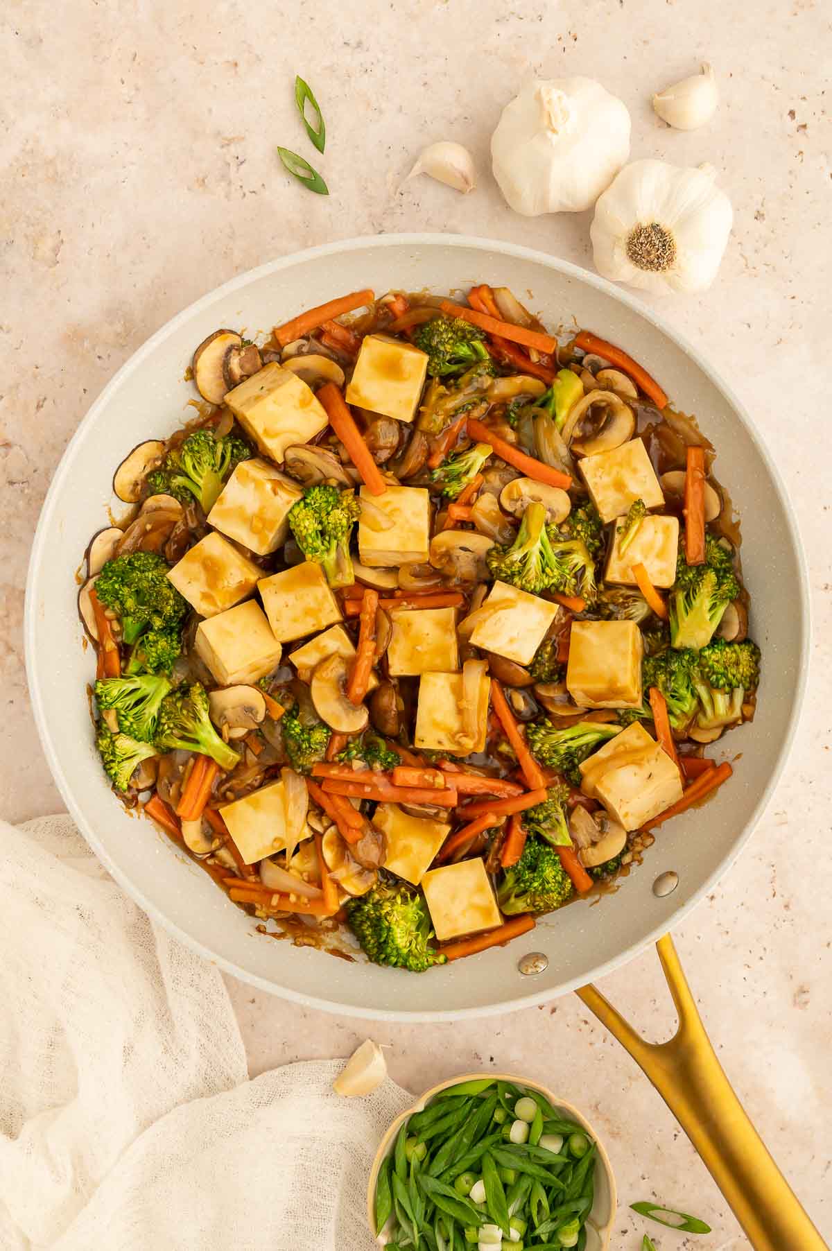 Cubed tofu added to a skillet of stir fry vegetables and glossy teriyaki sauce.