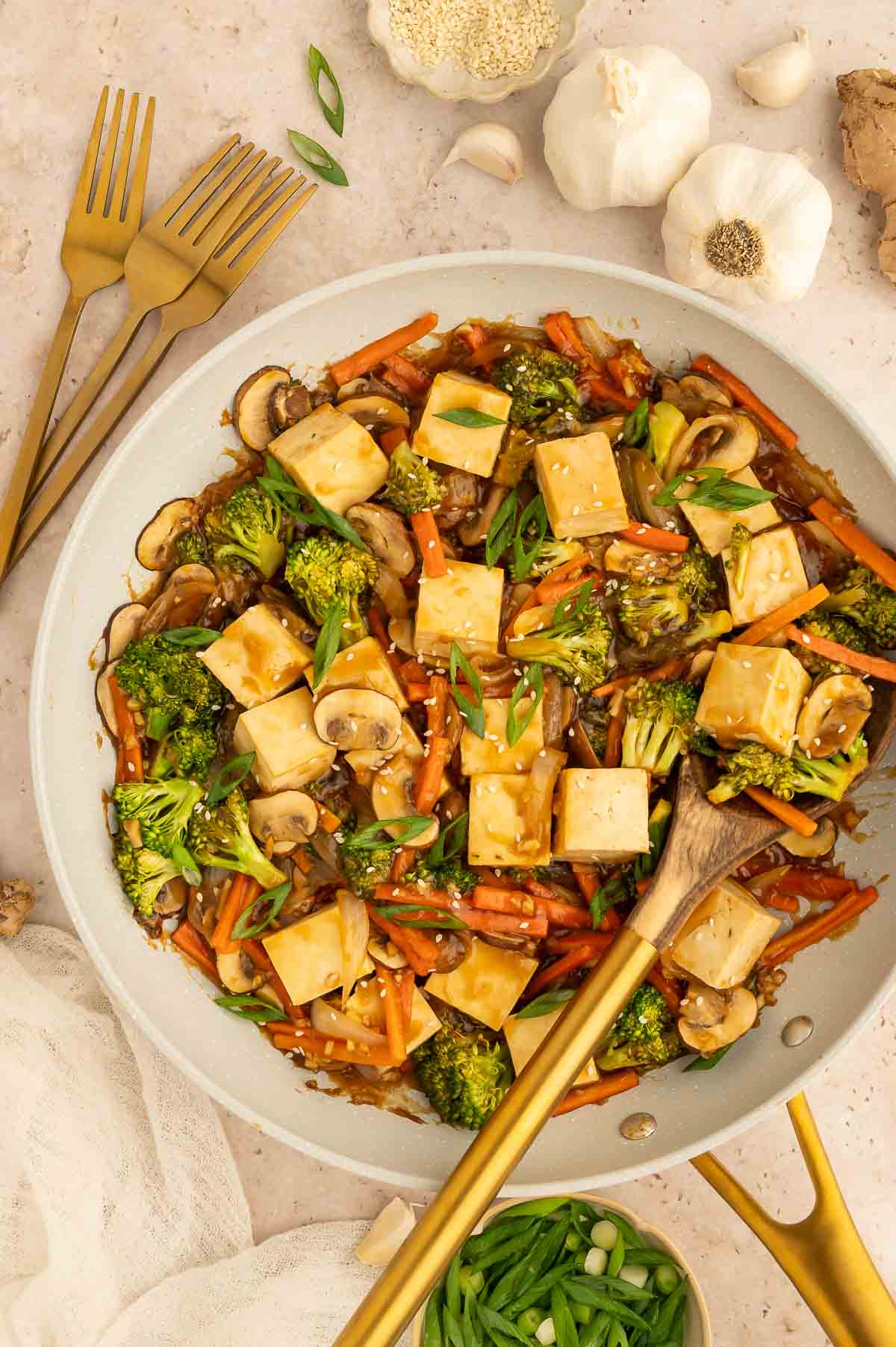 Tofu and vegetable teriyaki stir fry in a skillet with sesame seeds and scallions.