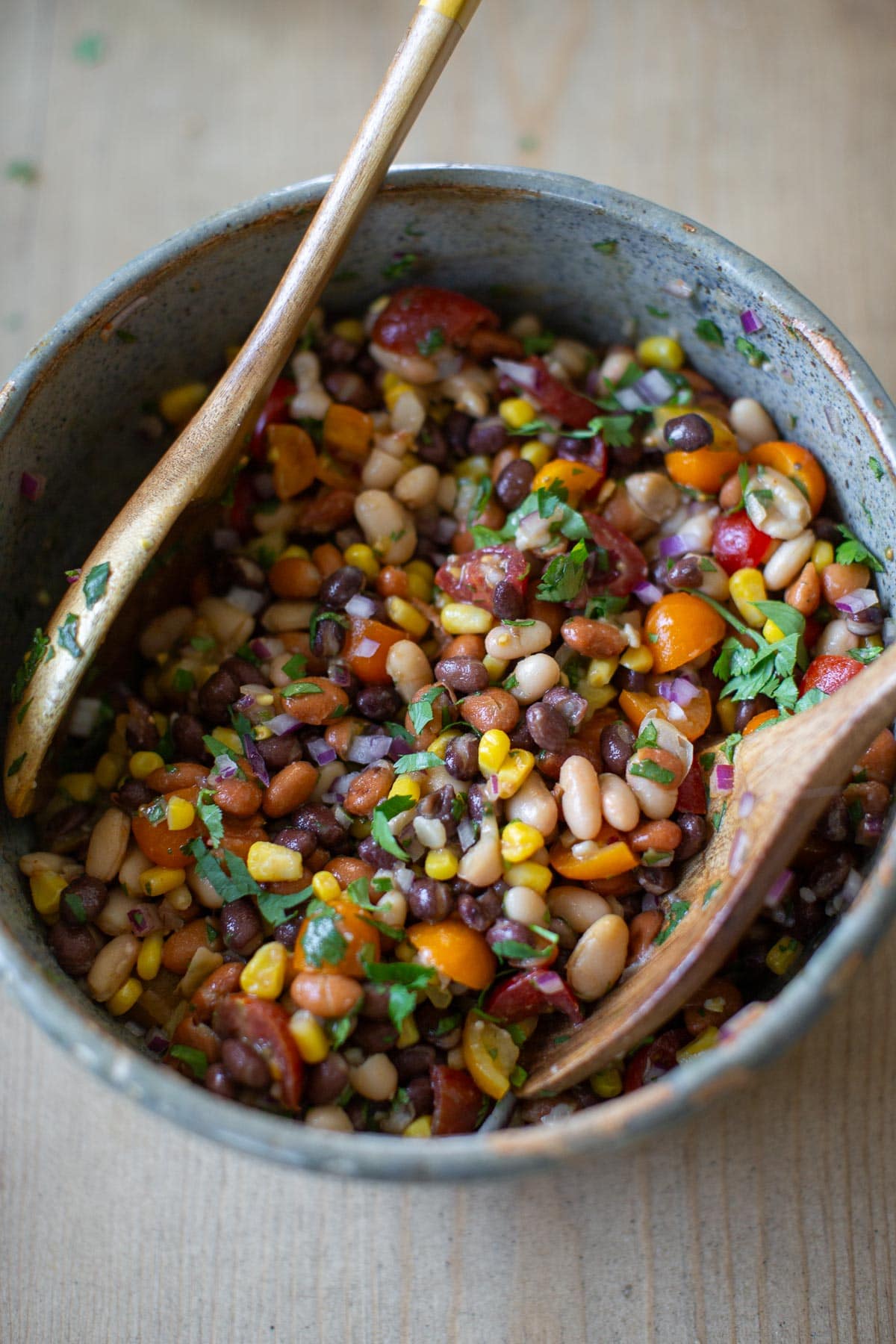 Three bean vegan salad after all the ingredients have been tossed together in a large bowl with wood spoons.