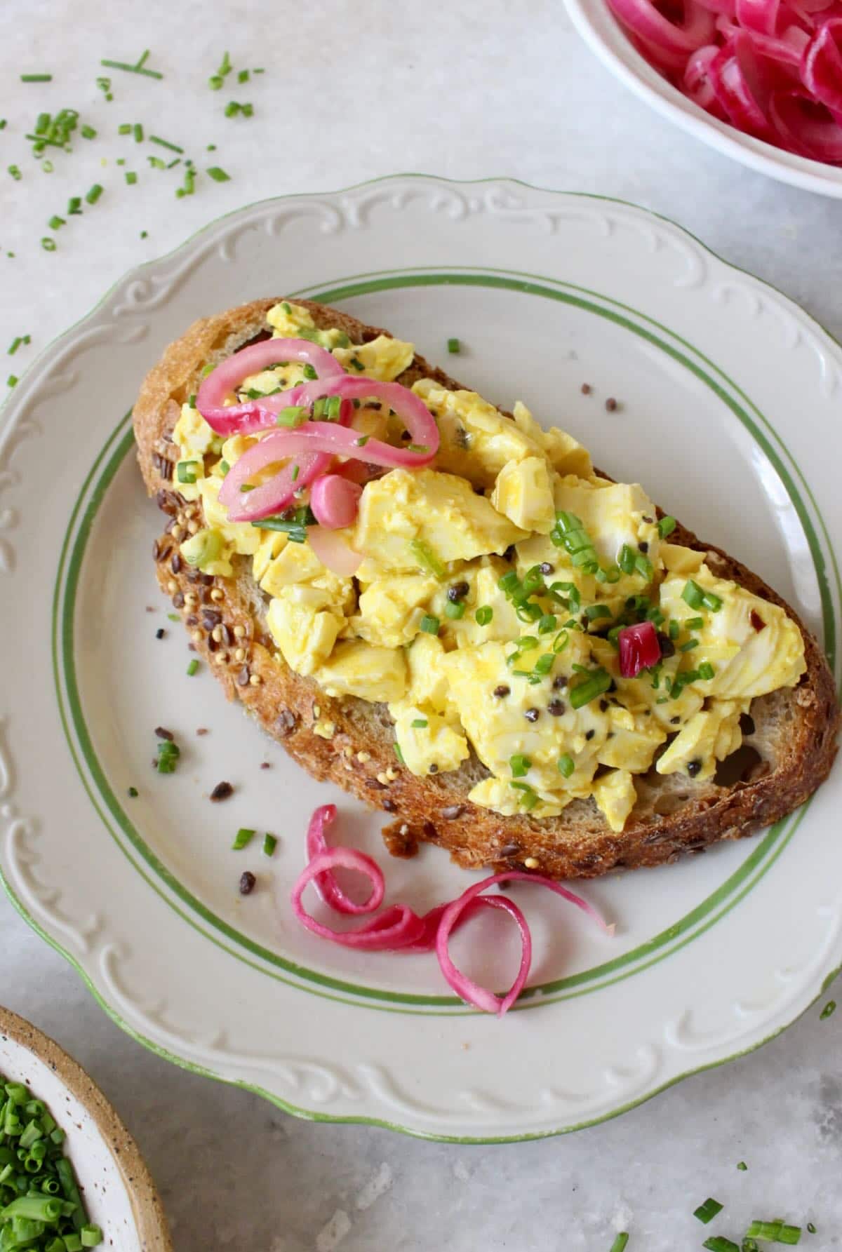 A slice of toast topped with tofu egg salad, pickled red onion, and chives.