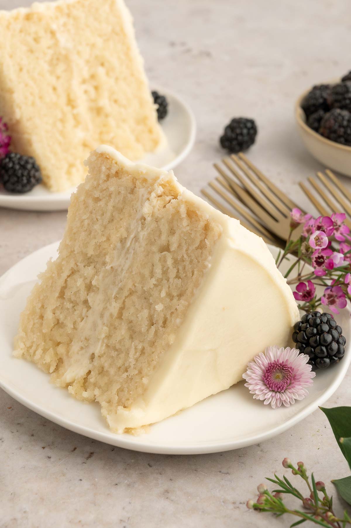 A piece of cake on a plate with berries and flowers.