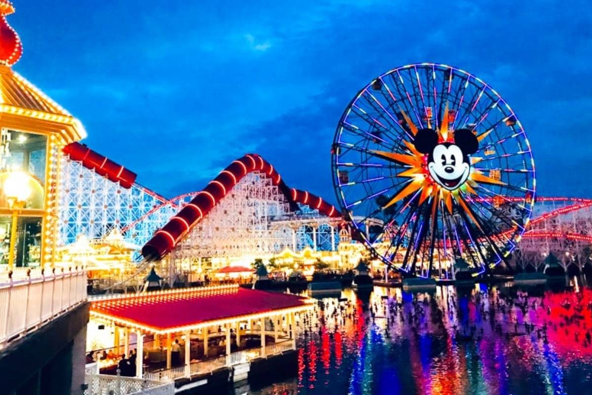 Nighttime view of California Adventure with the Mickey Ferris wheel lit up in bright colors, reflecting on the water, capturing the park’s vibrant atmosphere.