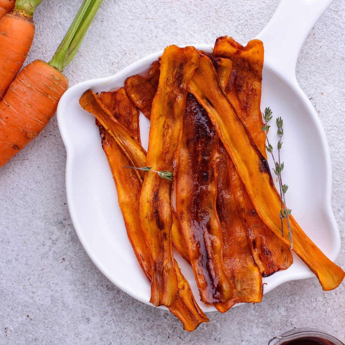 Sliced of vegan bacon made from carrots on a plate, beside a bunch of carrots.