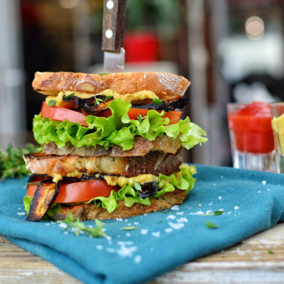 Two vegan BLT sandwiches stacked on one another with a knife holding them in place.