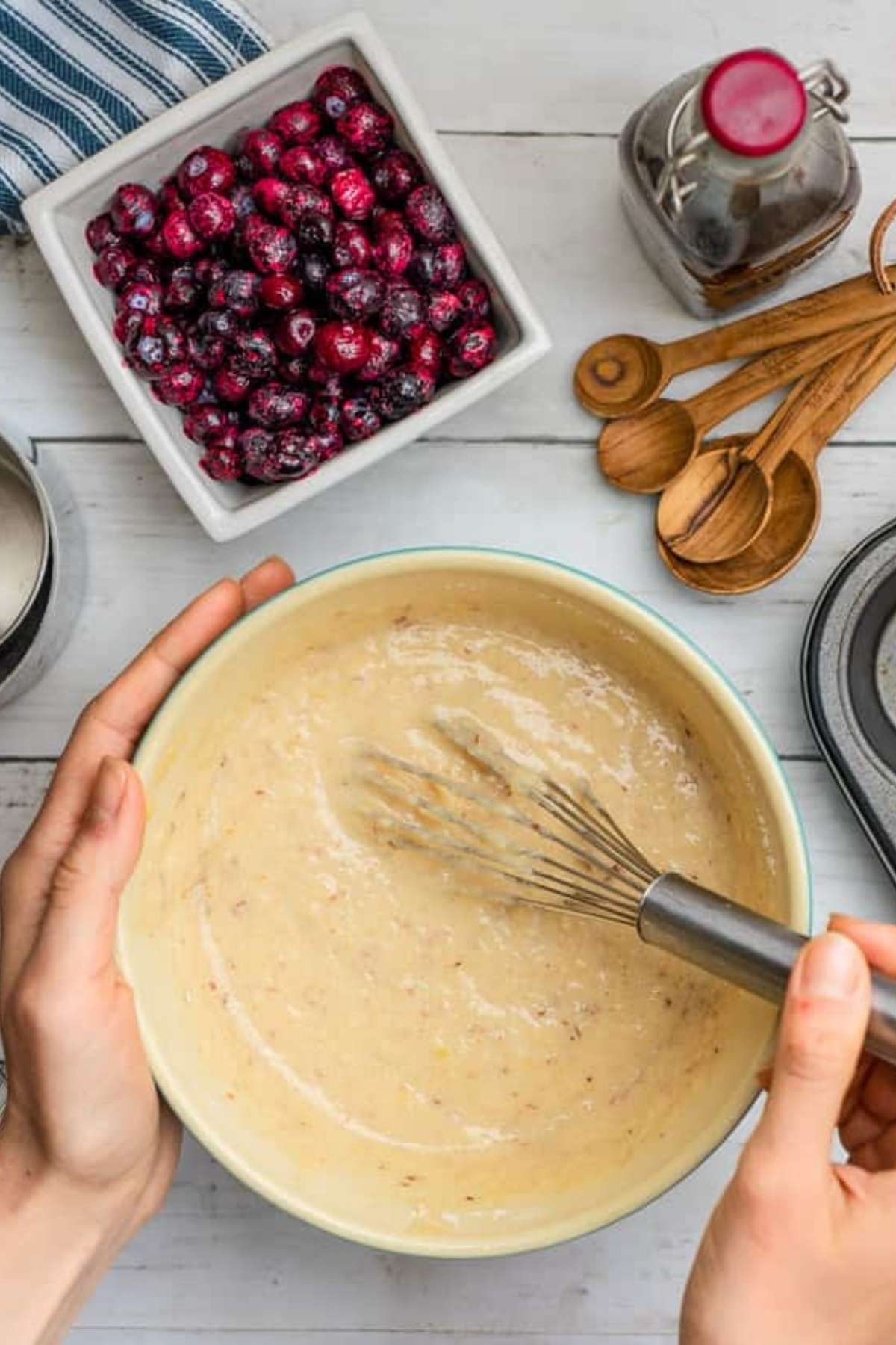 Hands stirring a bowl of blueberry muffin batter.