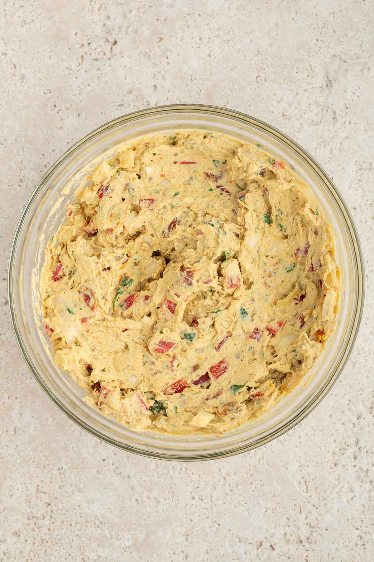 Sun-dried tomatoes, artichoke hearts, and spinach, onion, bell pepper, and garlic added into the tofu mixture in a large bowl.