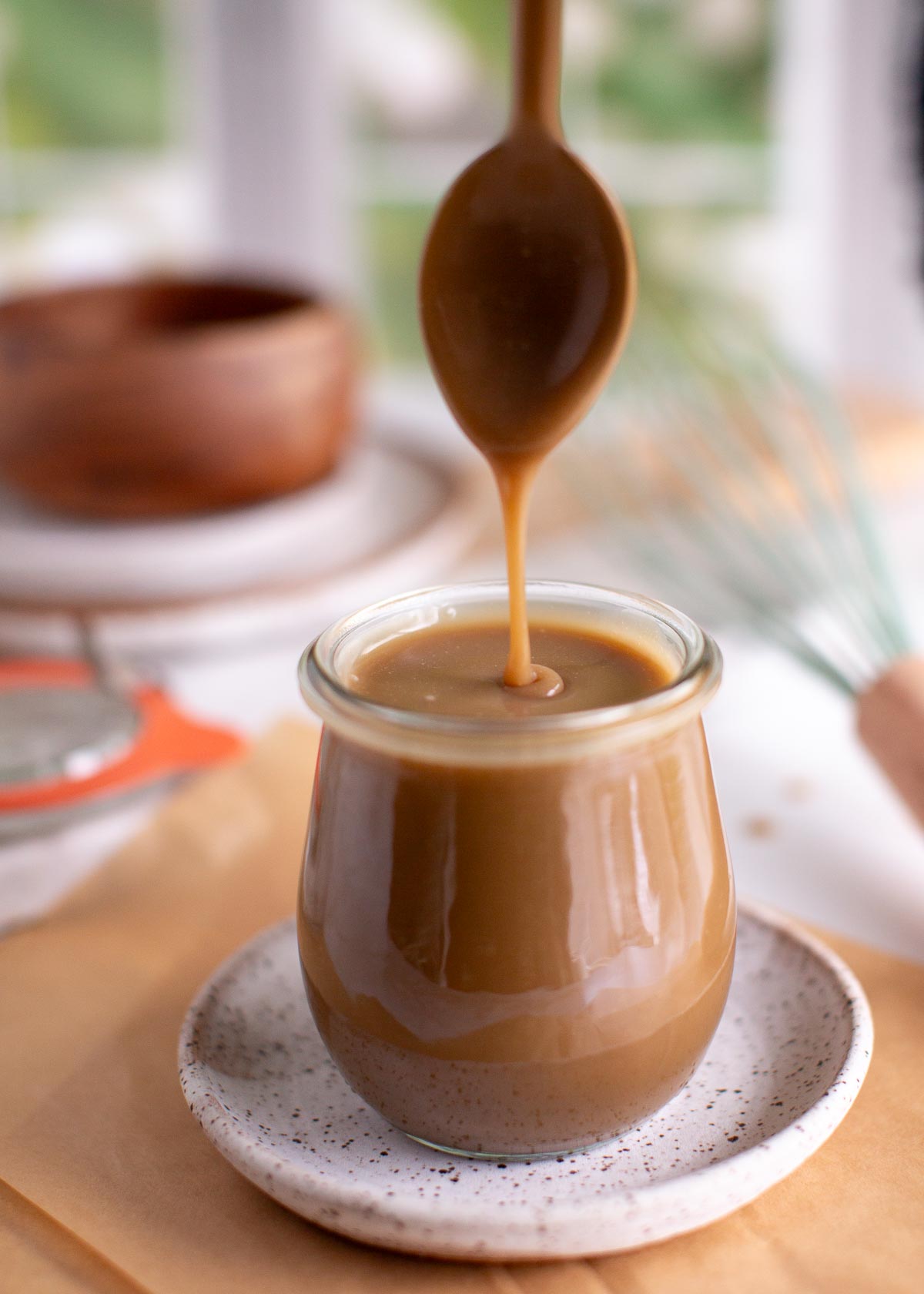 Vegan caramel sauce in a jar with a spoon dripping sauce off of it.