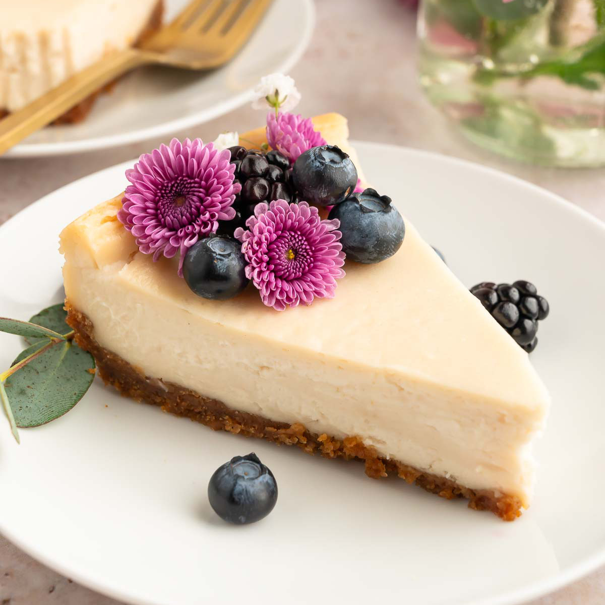 A slice of vegan cheesecake on a plate, topped with fresh berries and edible flowers.