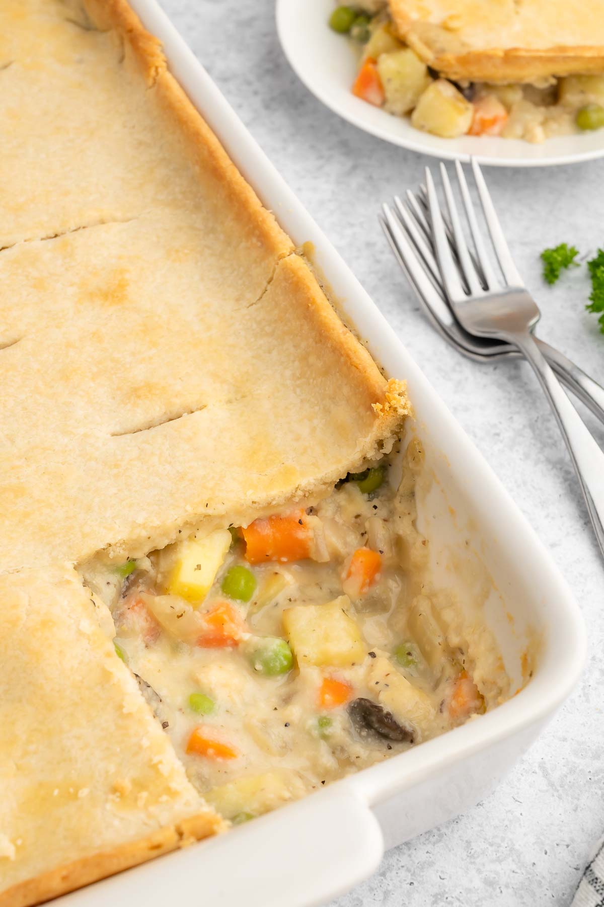 Vegan chicken pot pie in a casserole dish with a slice of the crust missing, revealing the vegetable filling.