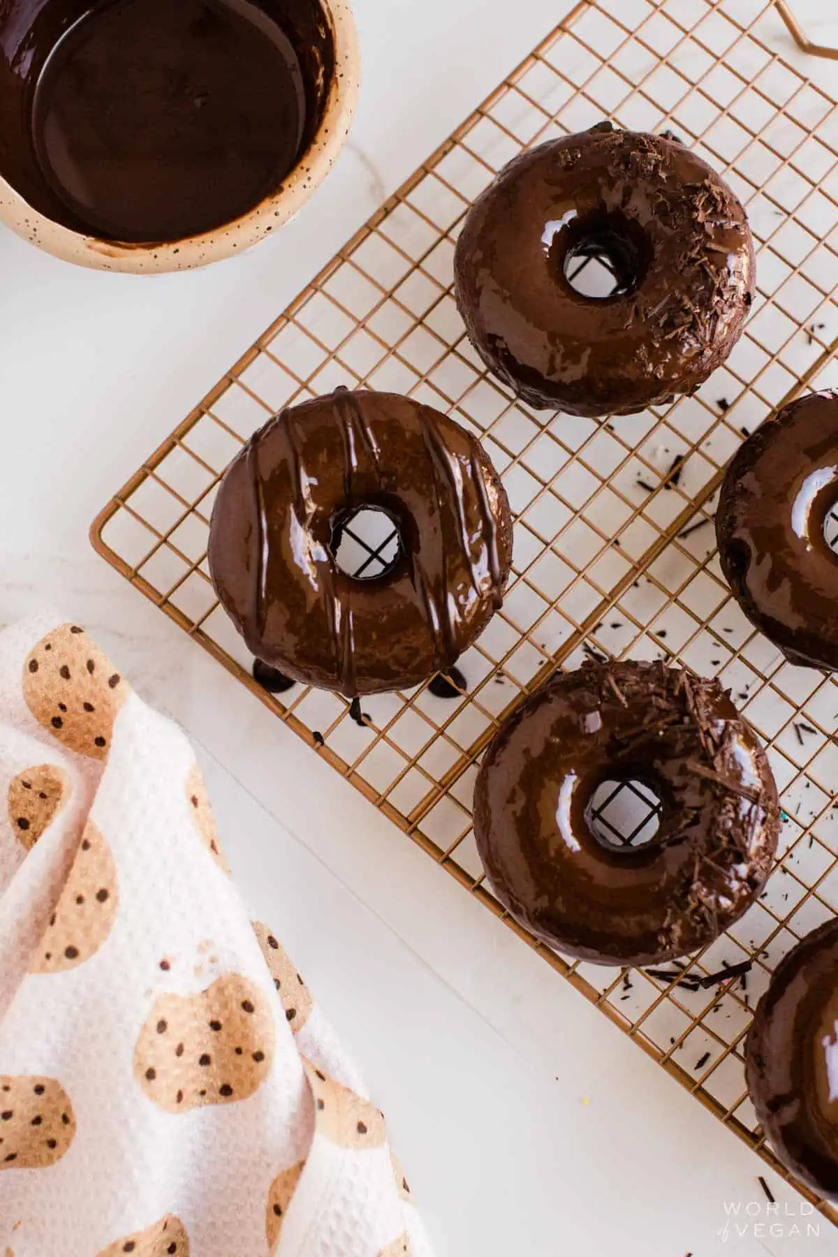 Decorated vegan chocolate donuts on cooling rack with a cookie pattern kitchen cloth.