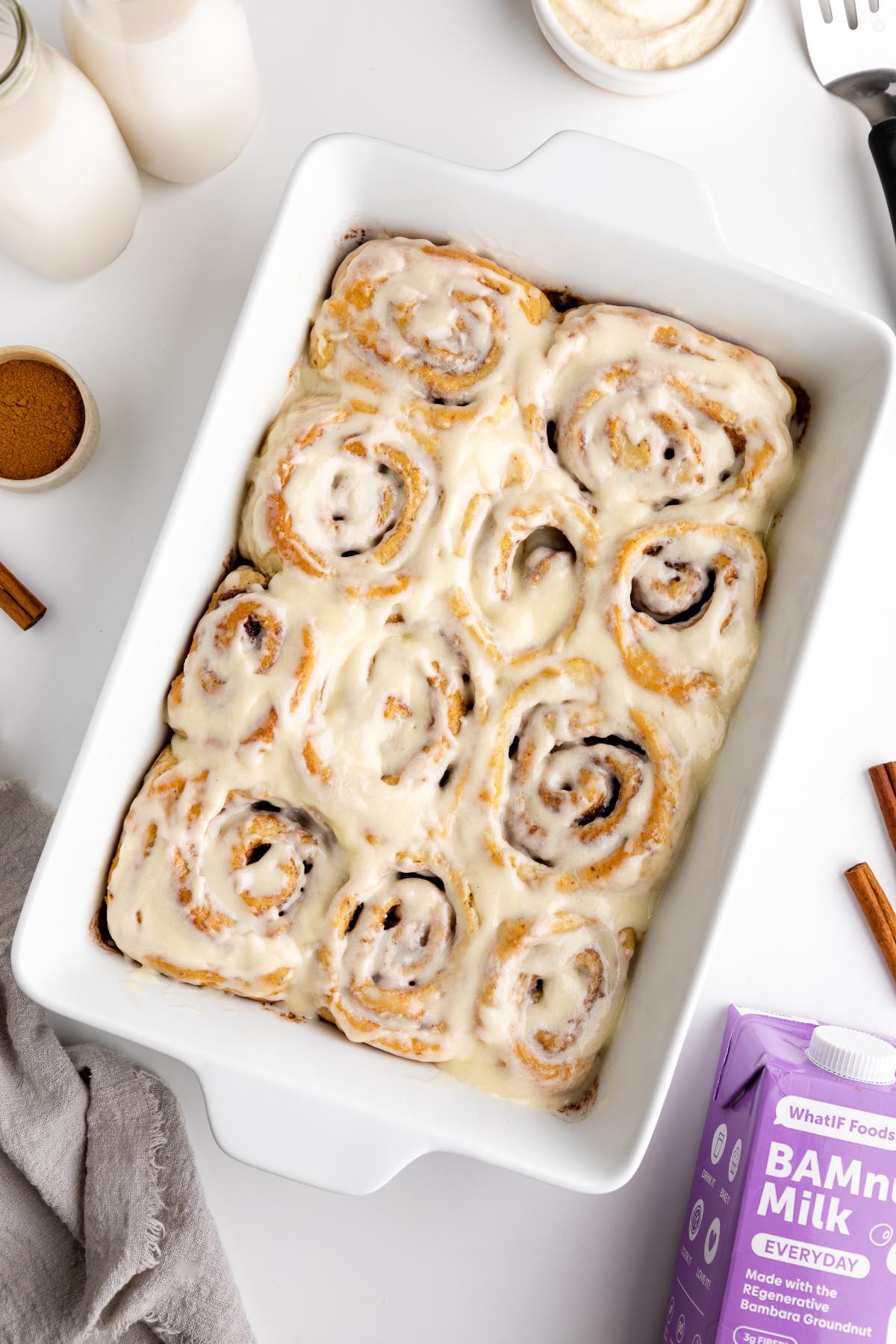 A flatlay of homemade baked vegan cinnamon rolls with icing in a white baking dish.