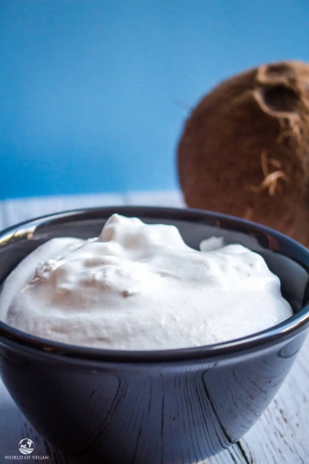 Coconut Whipped Cream in a blue bowl next to a fresh whole coconut.