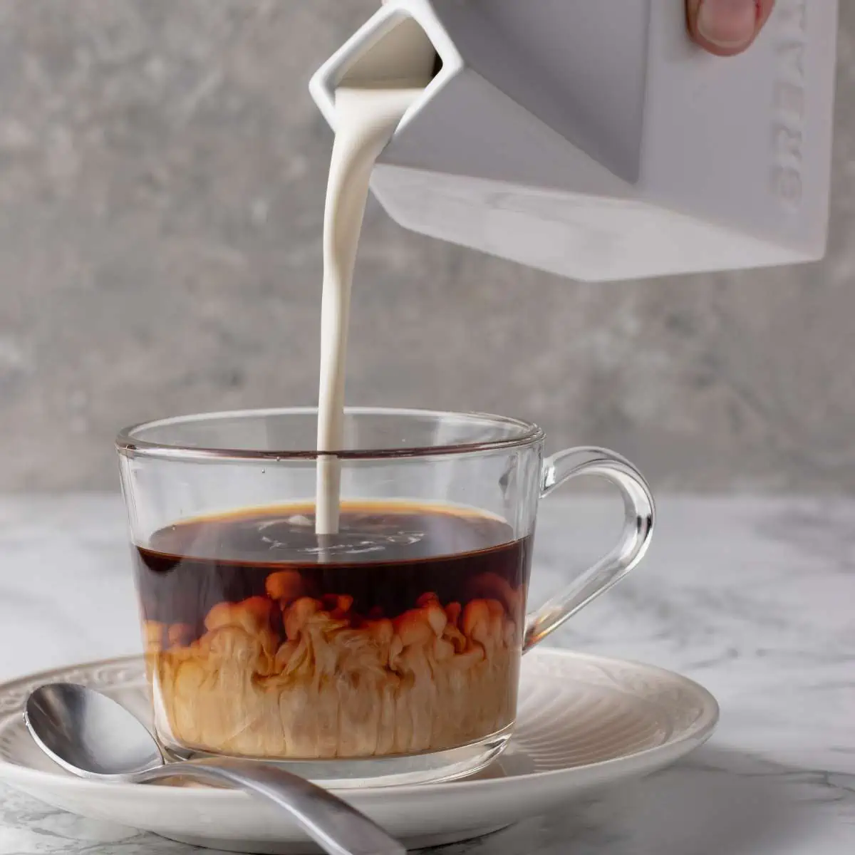 Pouring vegan coffee creamer into a glass of coffee.