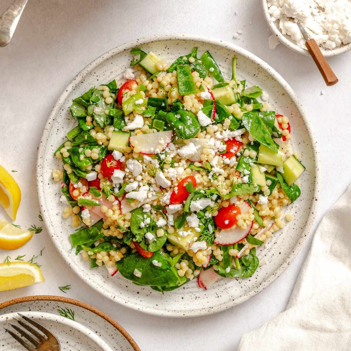 Overhead view of Israeli couscous salad with radish, spinach, cherry tomatoes, and a sprinkle of vegan feta cheese.