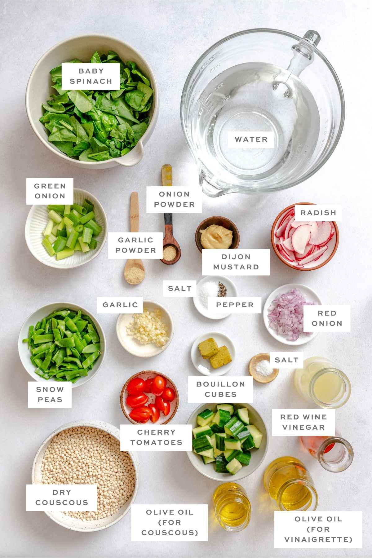 Labeled ingredients for vegan couscous salad, including spinach, tomatoes, cucumber, spices, and vinaigrette components.