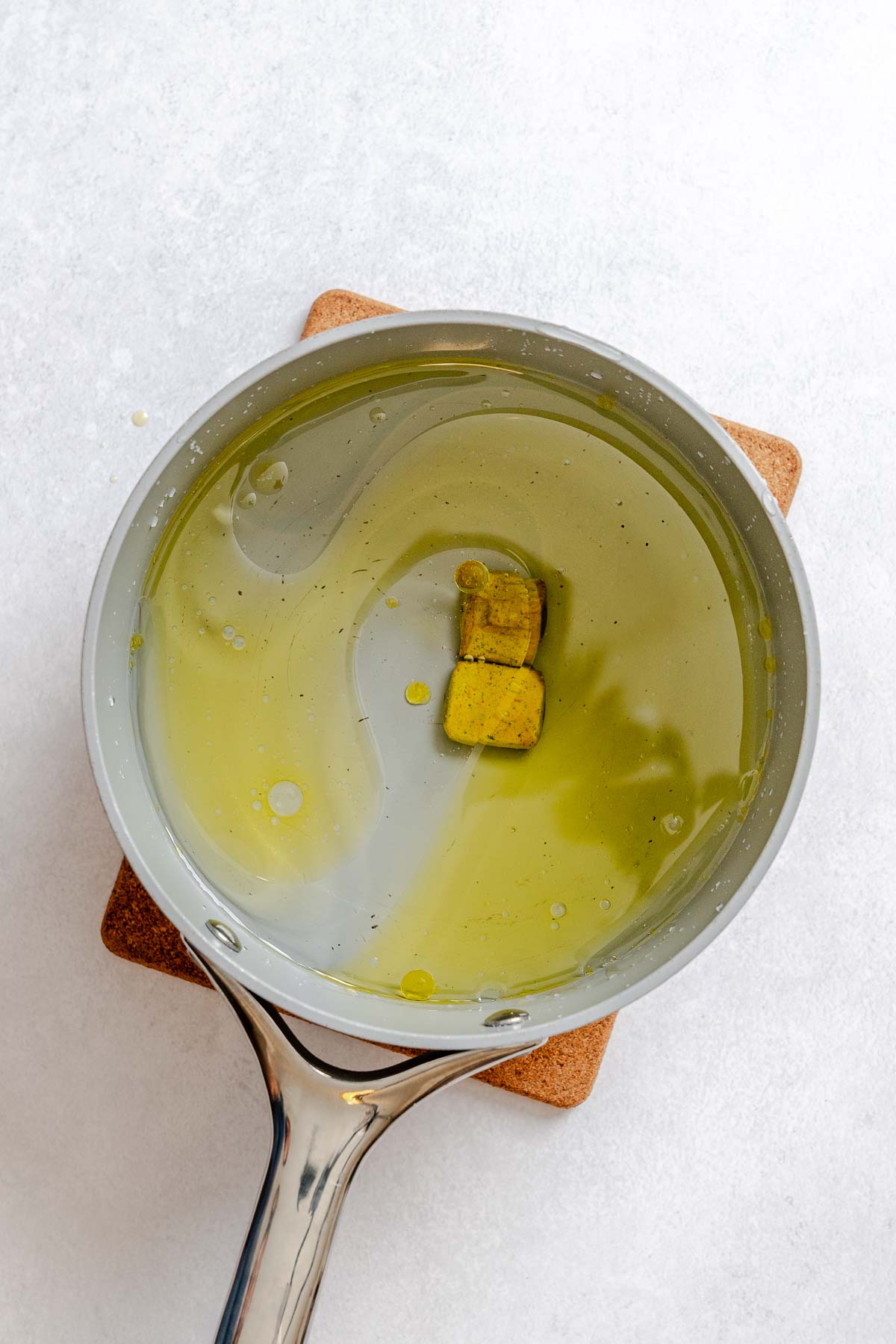 Olive oil and vegetable bouillon cubes in a saucepan, ready to cook Israeli couscous for a vegan salad base.