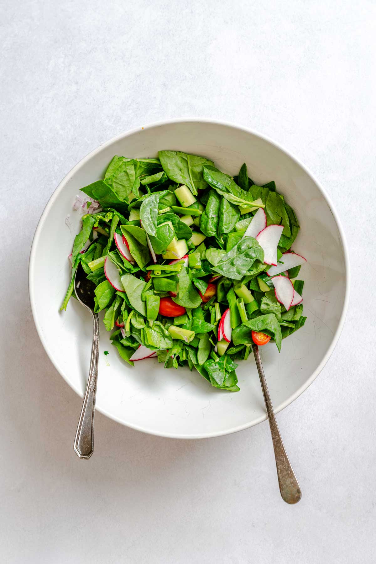 Fresh spinach, radish, tomatoes, and chopped vegetables mixed in a bowl before adding couscous.