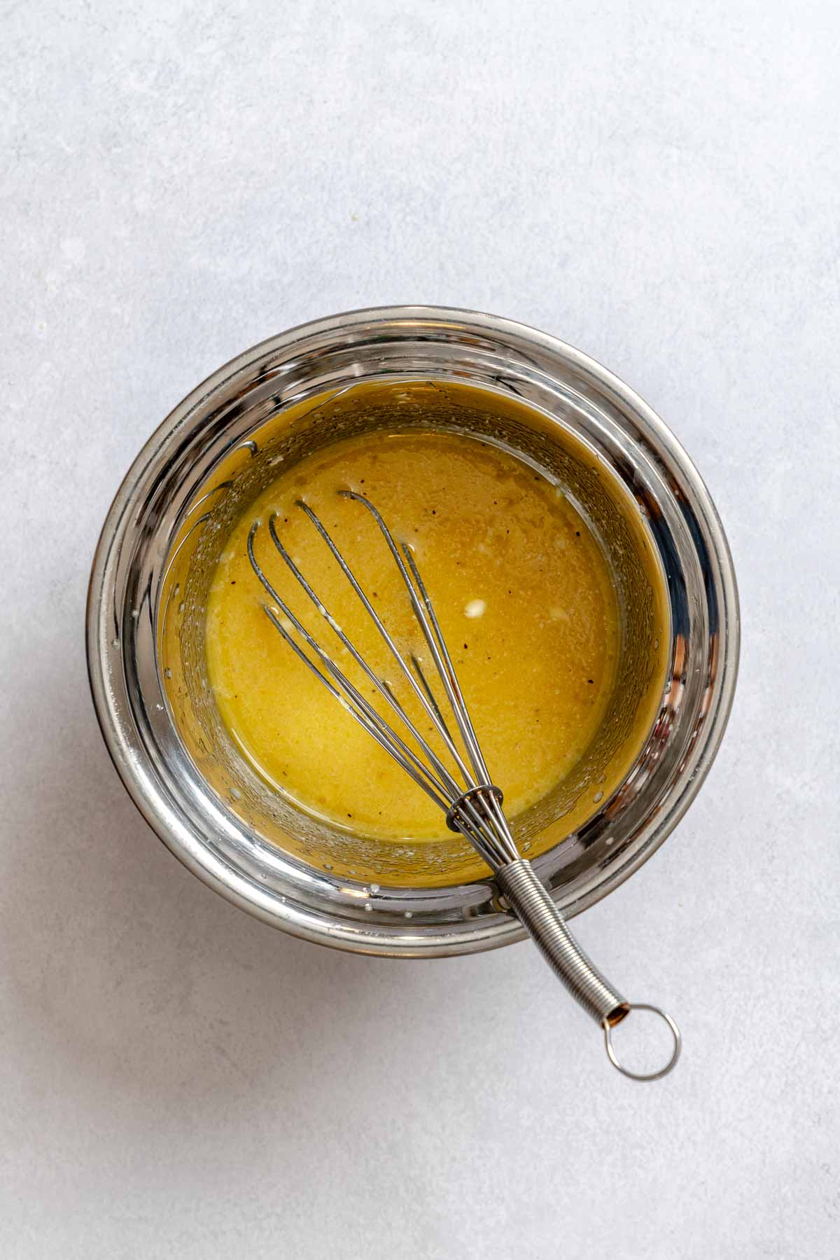 A stainless steel bowl and whisk with a homemade lemon vinaigrette dressing.