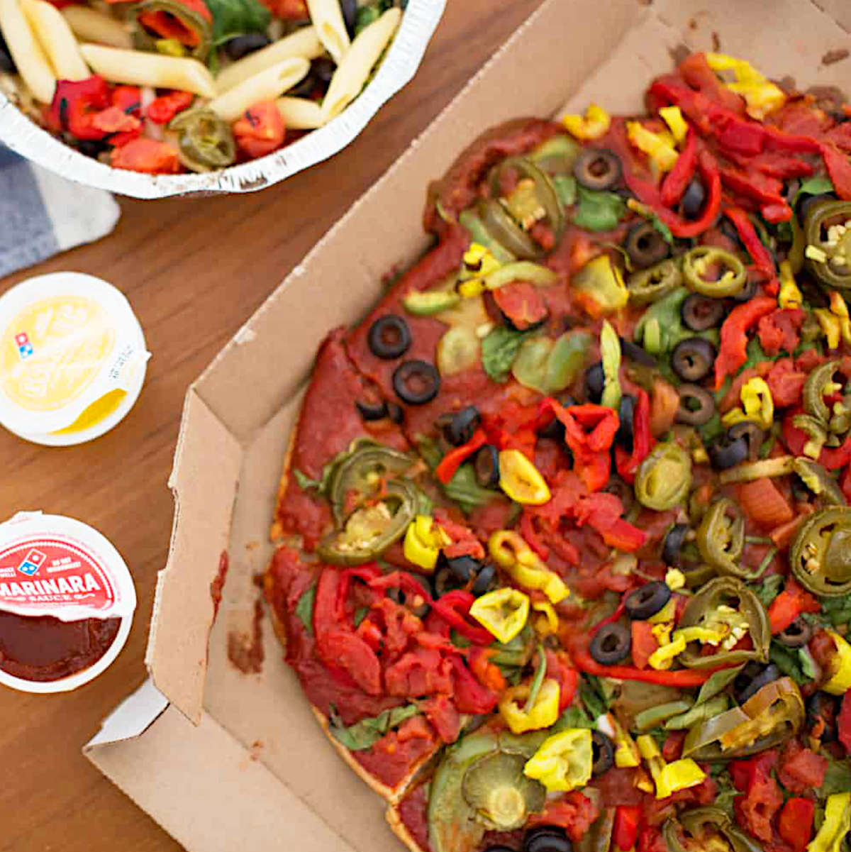 Vegan pizza from Domino's with a side of extra sauces and pasta salad.