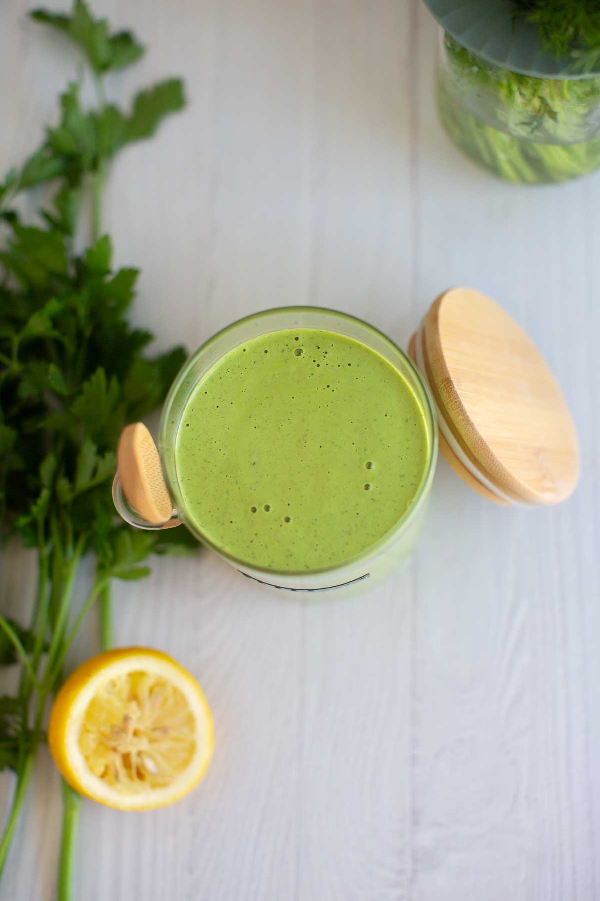 Vegan green goddess dressing in a glass jar with a wooden spoon and wooden sealable lid.