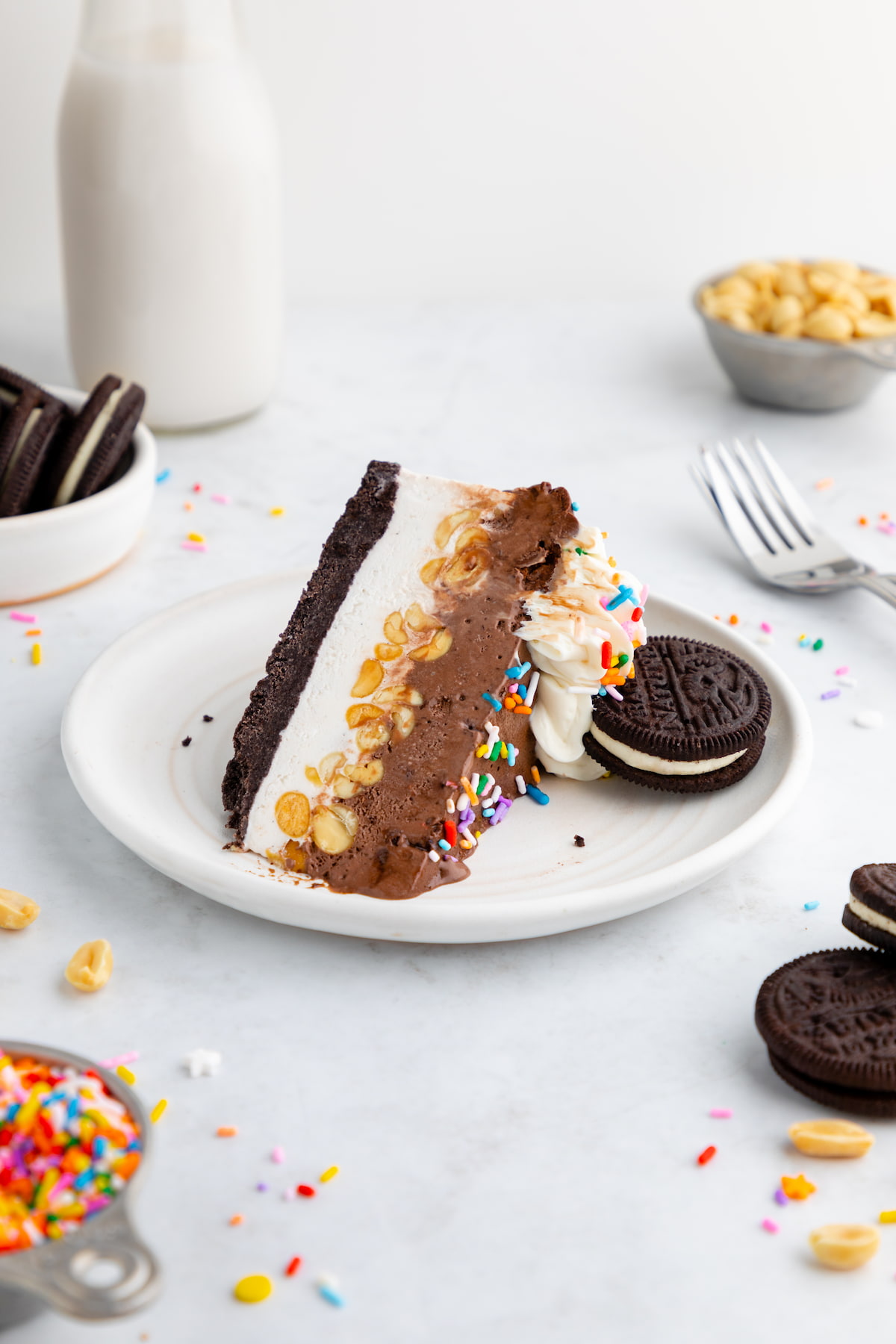 A slice of vegan ice cream cake on a serving plate, displaying the layer of ice cream, chopped nuts, and Oreo cookie crust.