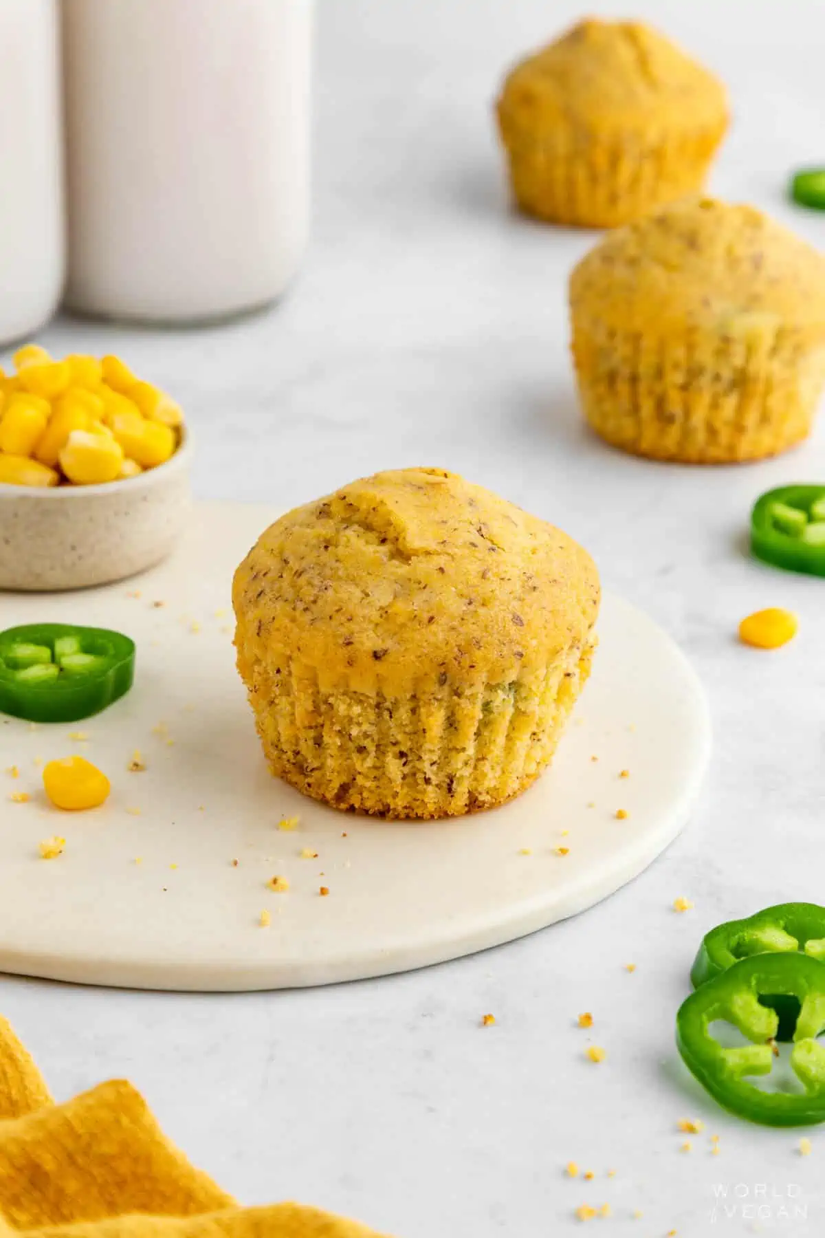 Fresh baked dairy-free cornbread muffins scattered on a table with jalapeno peppers.