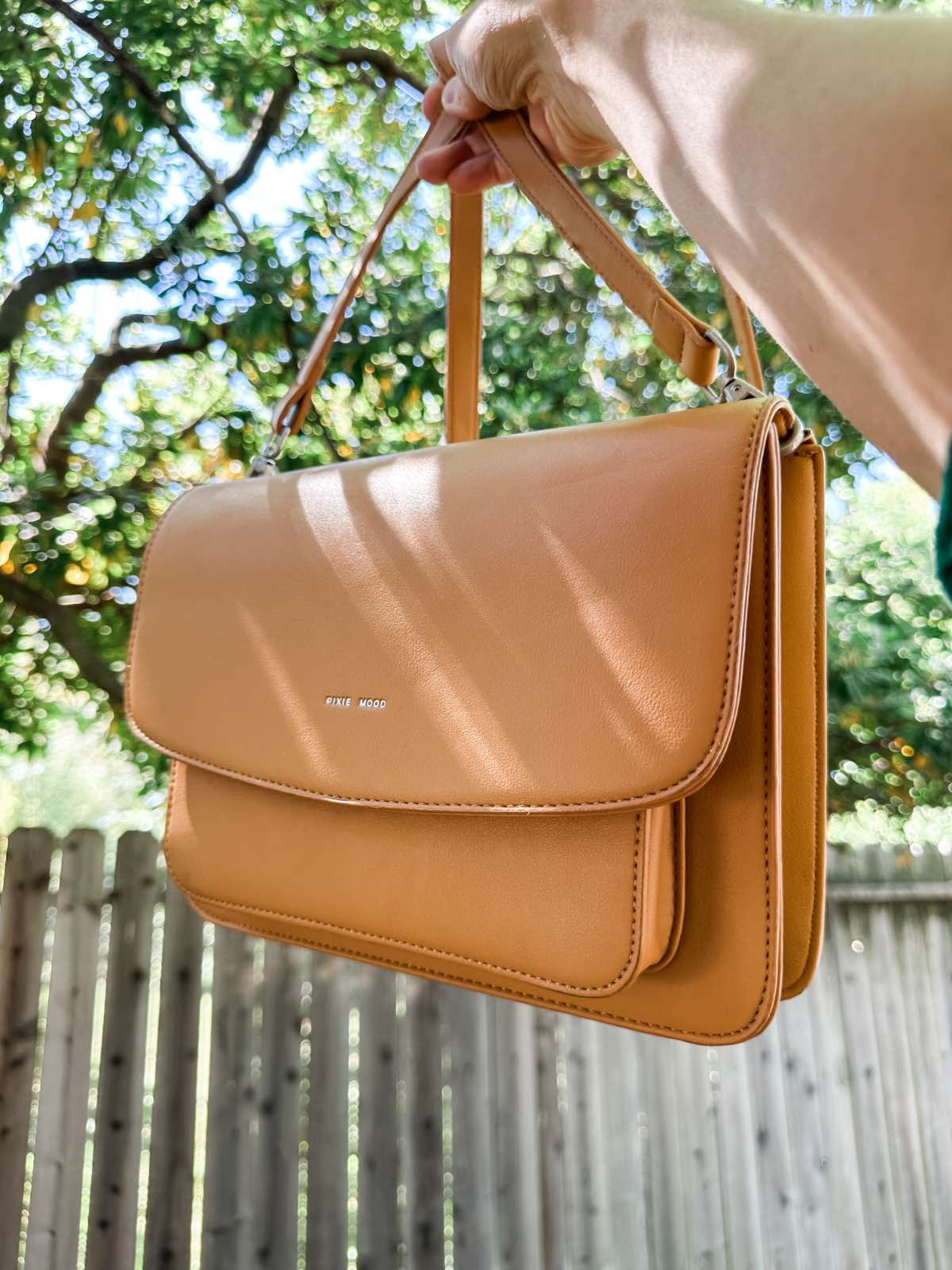 Woman holding out a tan vegan leather handbag purse from Pixie Mood.