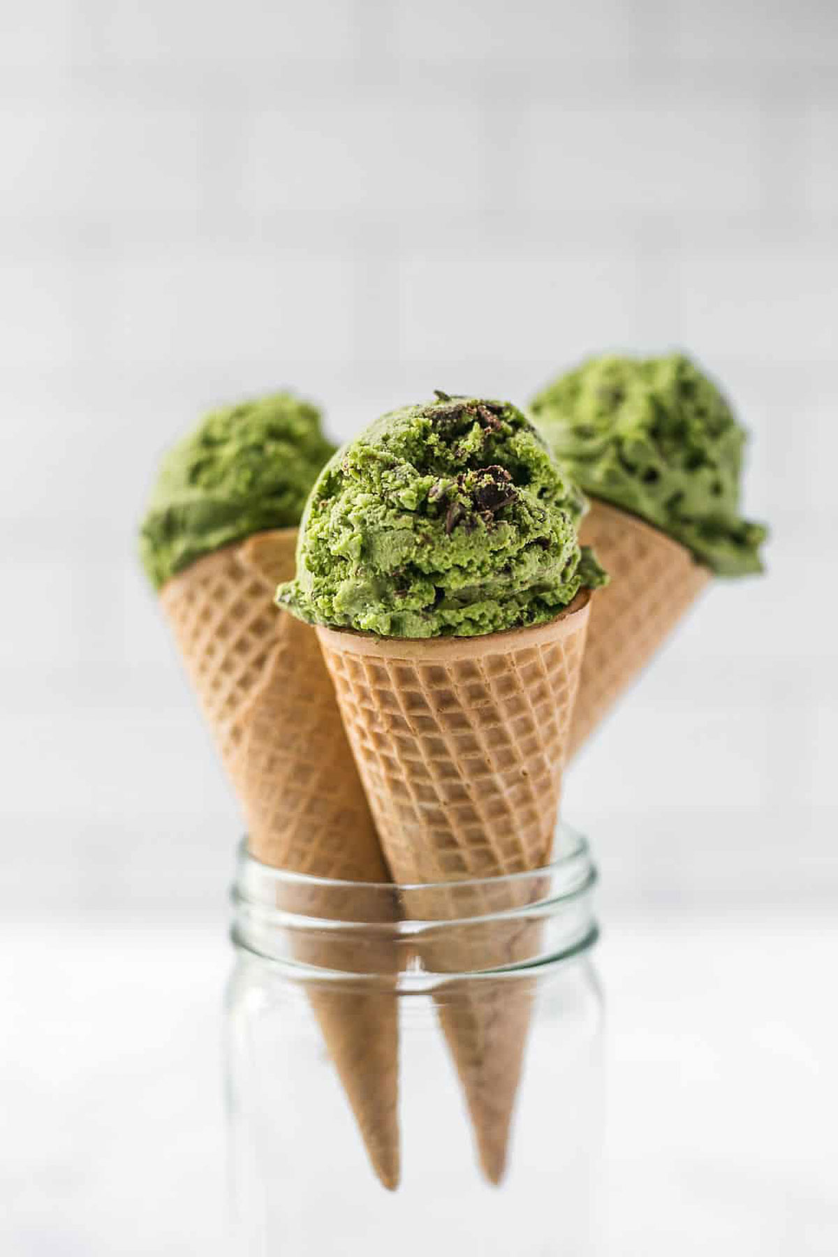 Three waffle cones filled with vegan matcha chocolate chip ice cream, styled in a glass jar.