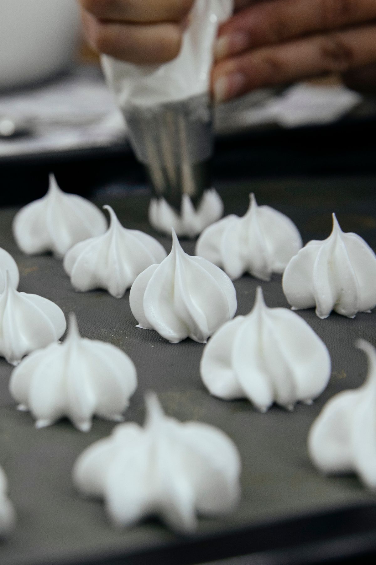 Vegan meringue mixture being piped onto a baking sheet in small decorative swirls, ready for baking.