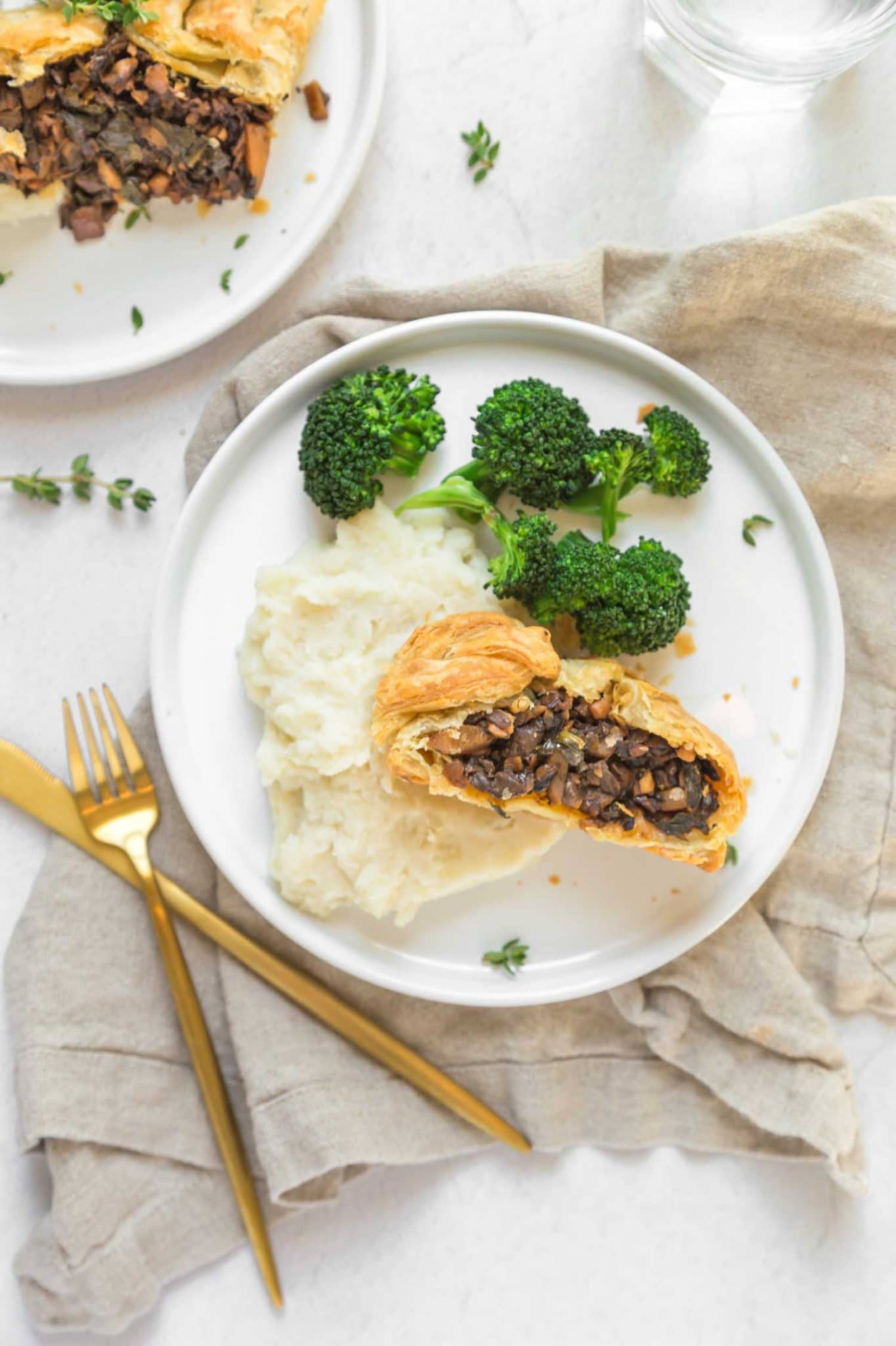 A slice of vegan mushroom Wellington on a plate with broccoli and mashed potatoes.