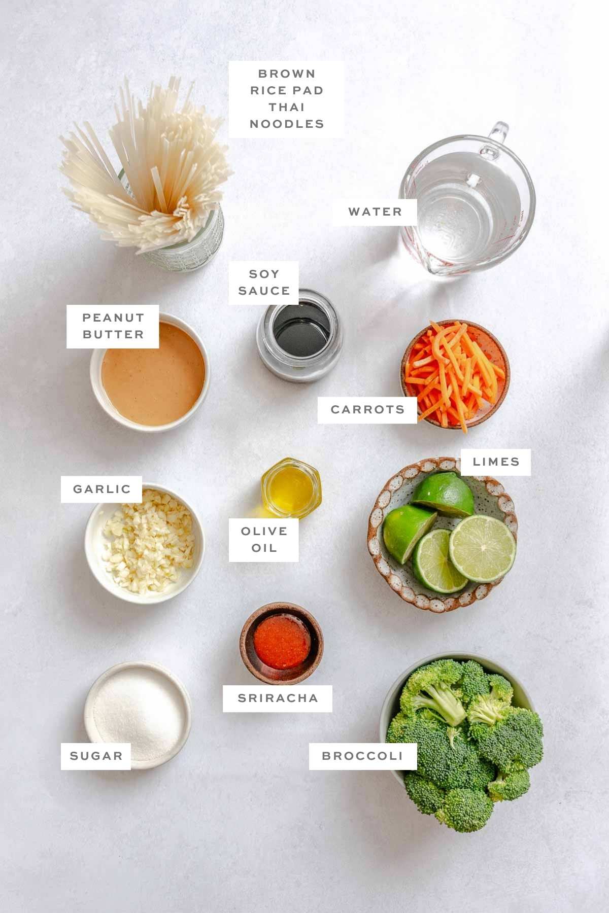 Ingredients for vegan pad Thai laid out with labels: rice noodles, peanut butter, soy sauce, veggies, garlic, lime, and Sriracha.