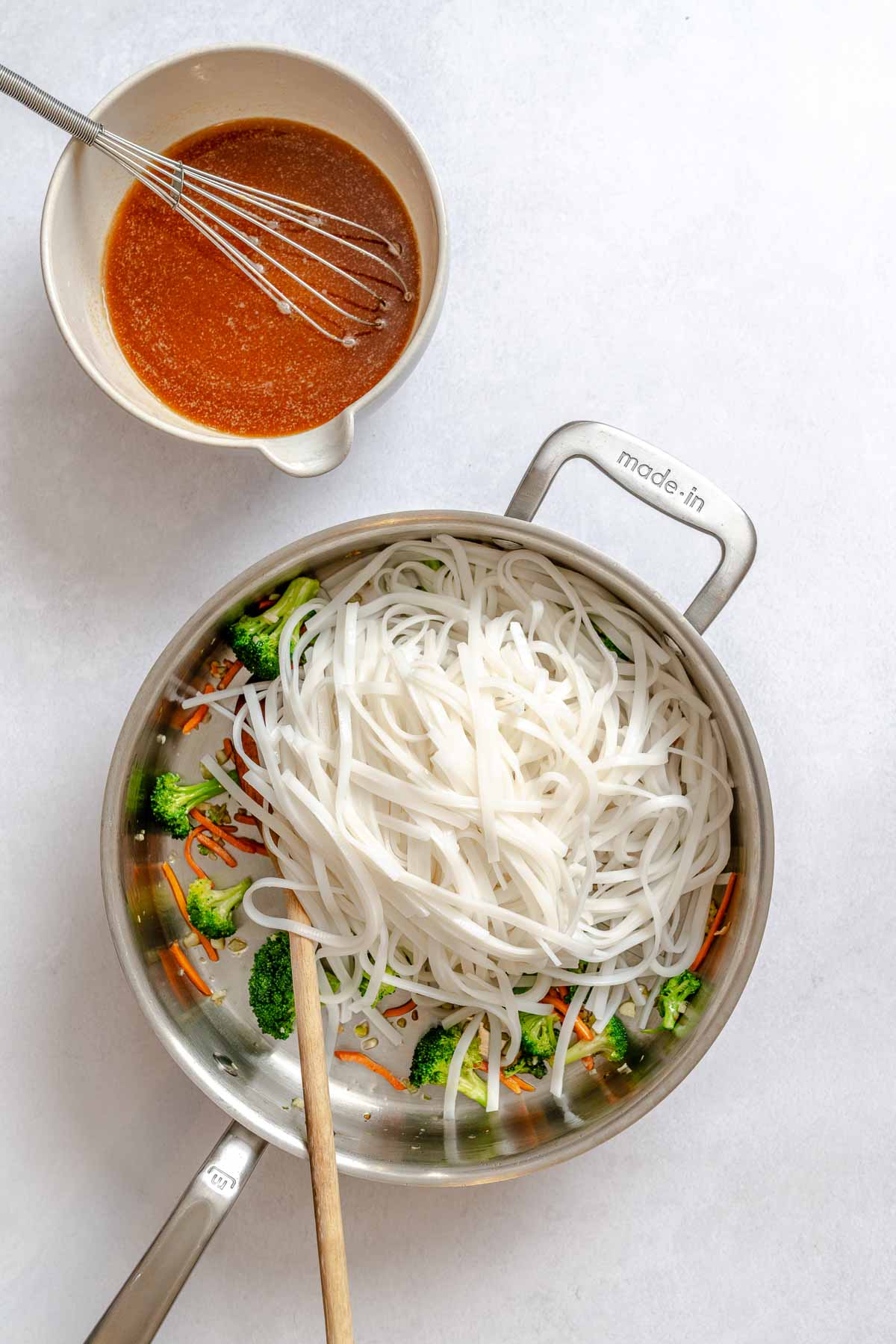 Soaked rice noodles added to sautéed vegetables in a skillet, ready for sauce.