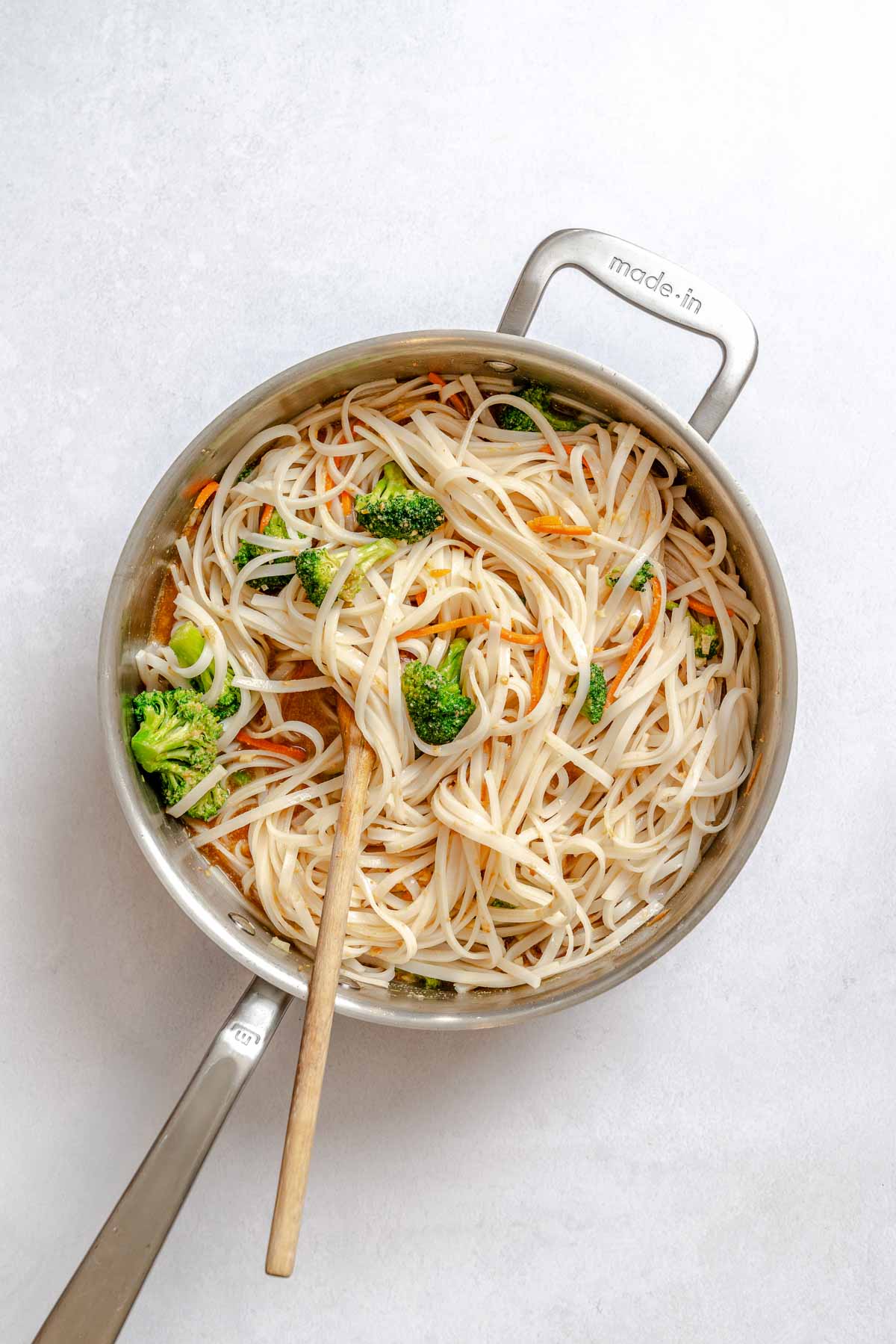 Vegan pad Thai noodles tossed with broccoli, carrots, and sauce in a skillet.