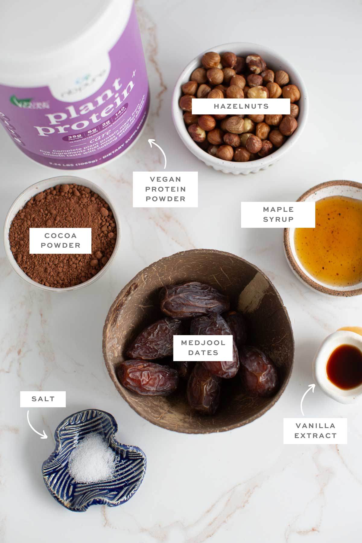 Gathered ingredients for vegan protein balls in individual bowls with labels.