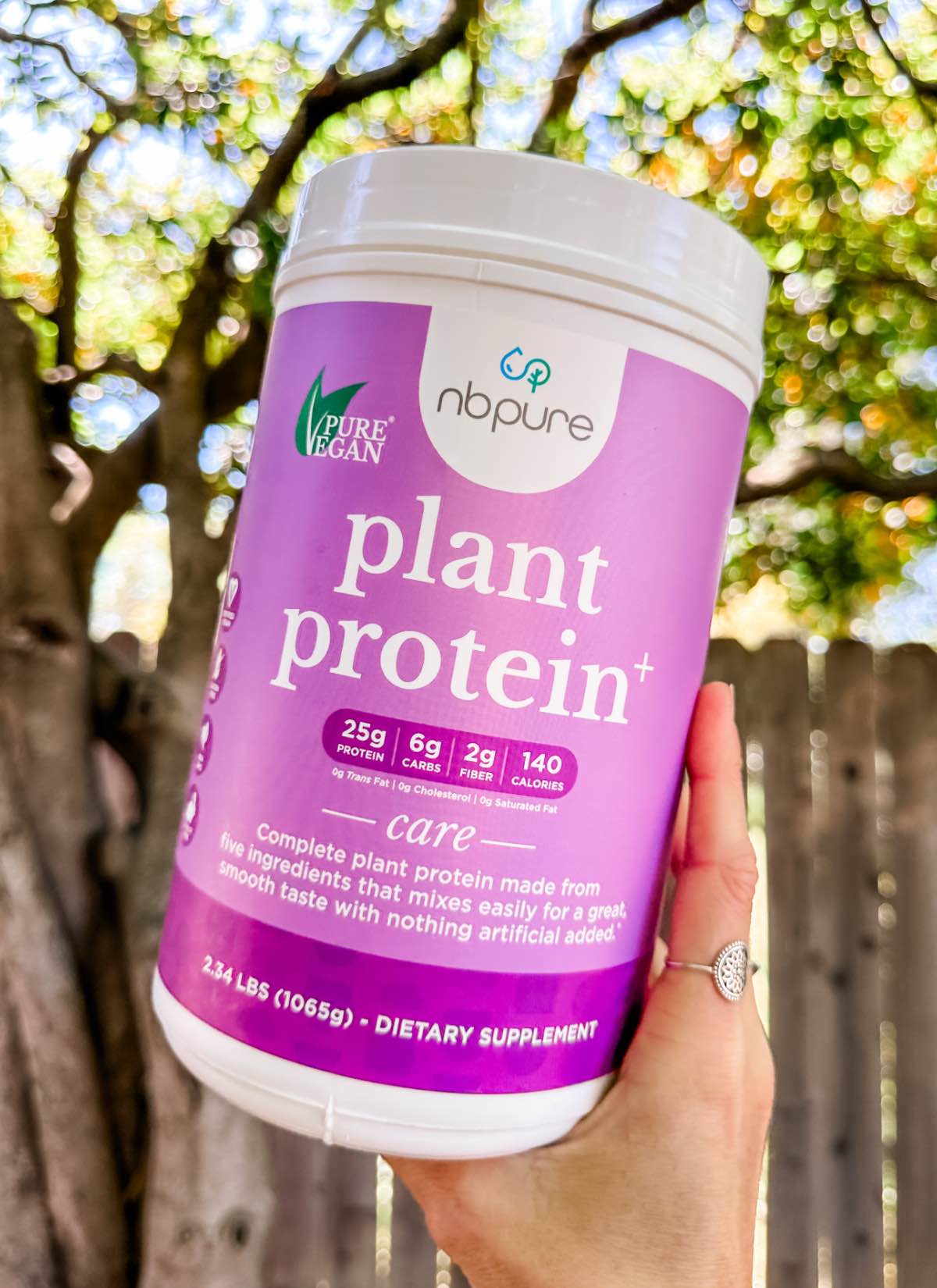 A purple container of the Plant Protein+ vegan protein powder from the brand NBPure held outside.
