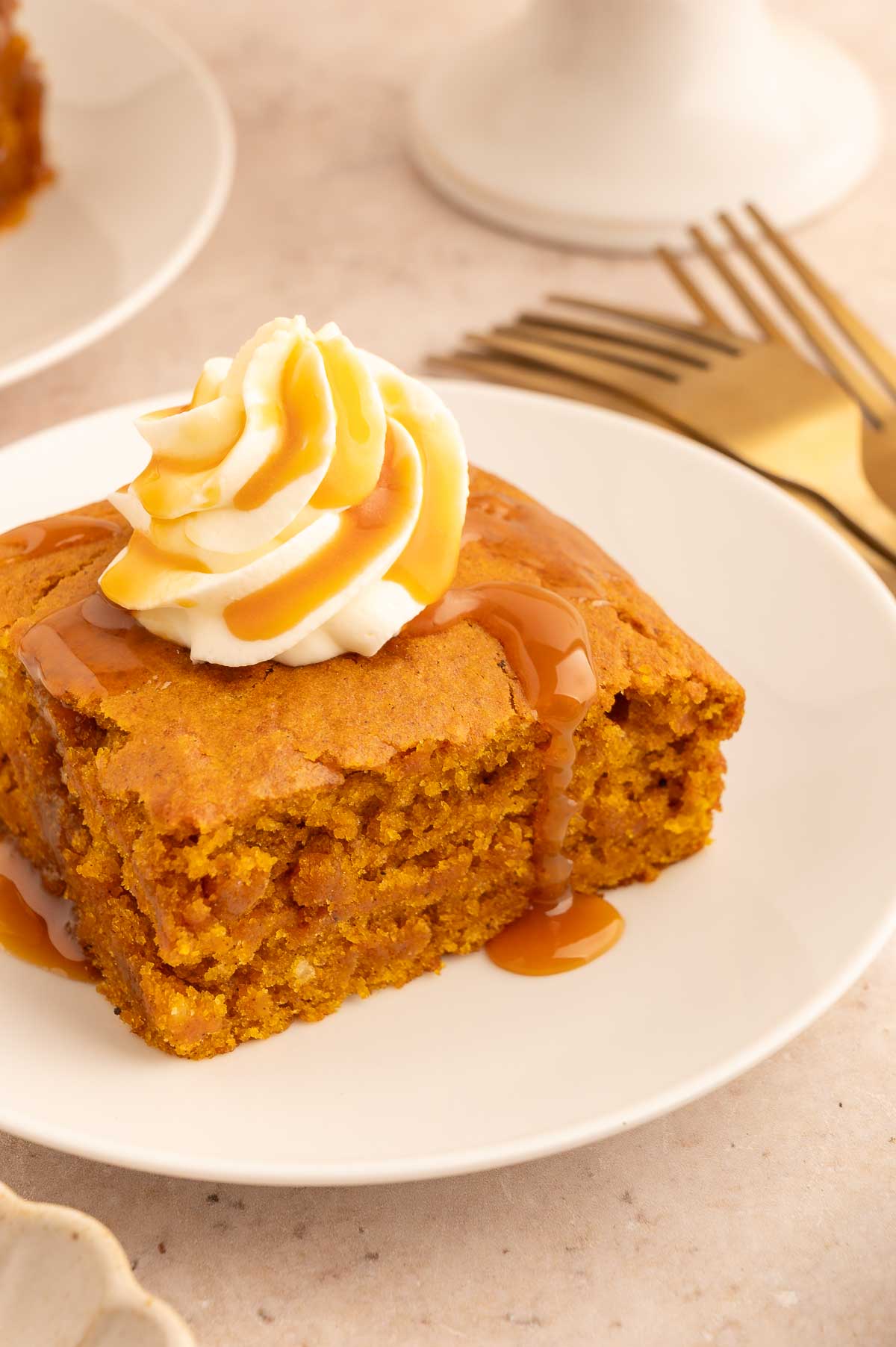 Moist vegan pumpkin cake square with whipped cream and caramel drizzle on white plate.