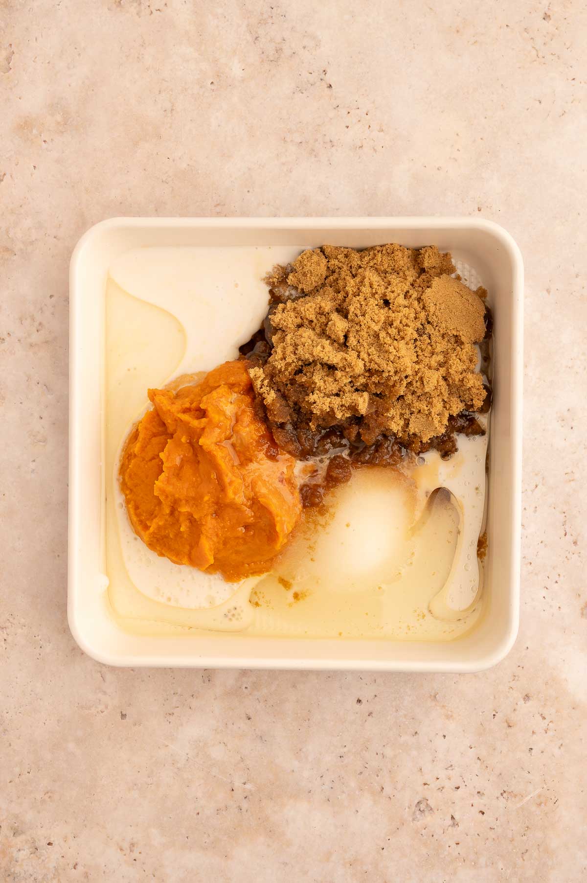 Wet ingredients for the pumpkin dump cake added to a baking dish.