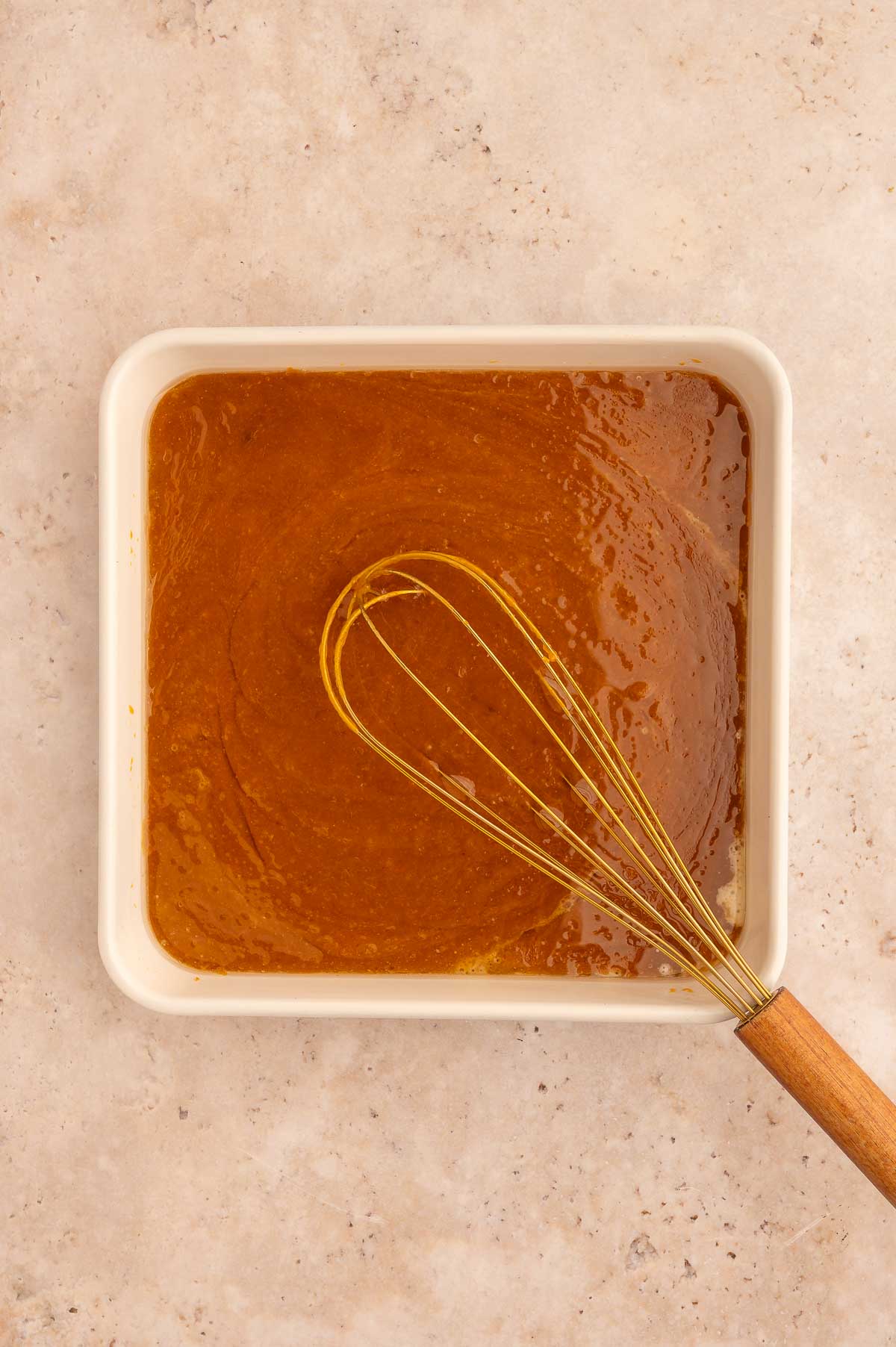Wet ingredients for the pumpkin dump cake all mixed together with a whisk in a baking dish.