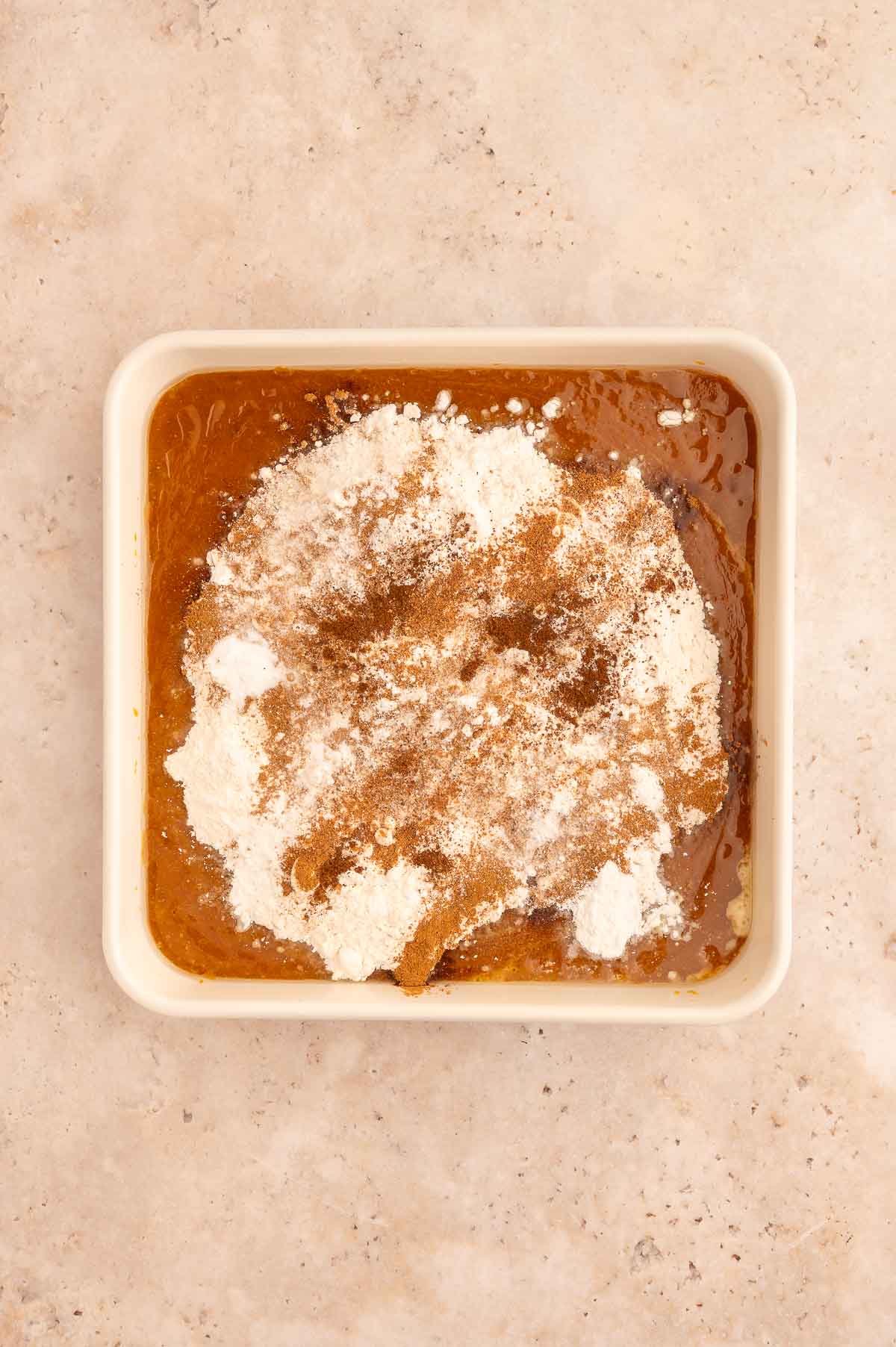 Dry ingredients added to the wet ingredients for the pumpkin dump cake in a baking dish.