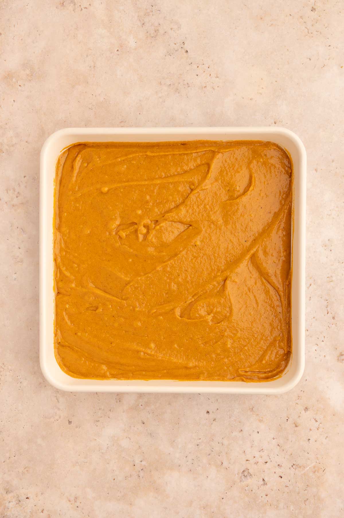 The batter for the vegan pumpkin dump cake all mixed together in a white baking dish.