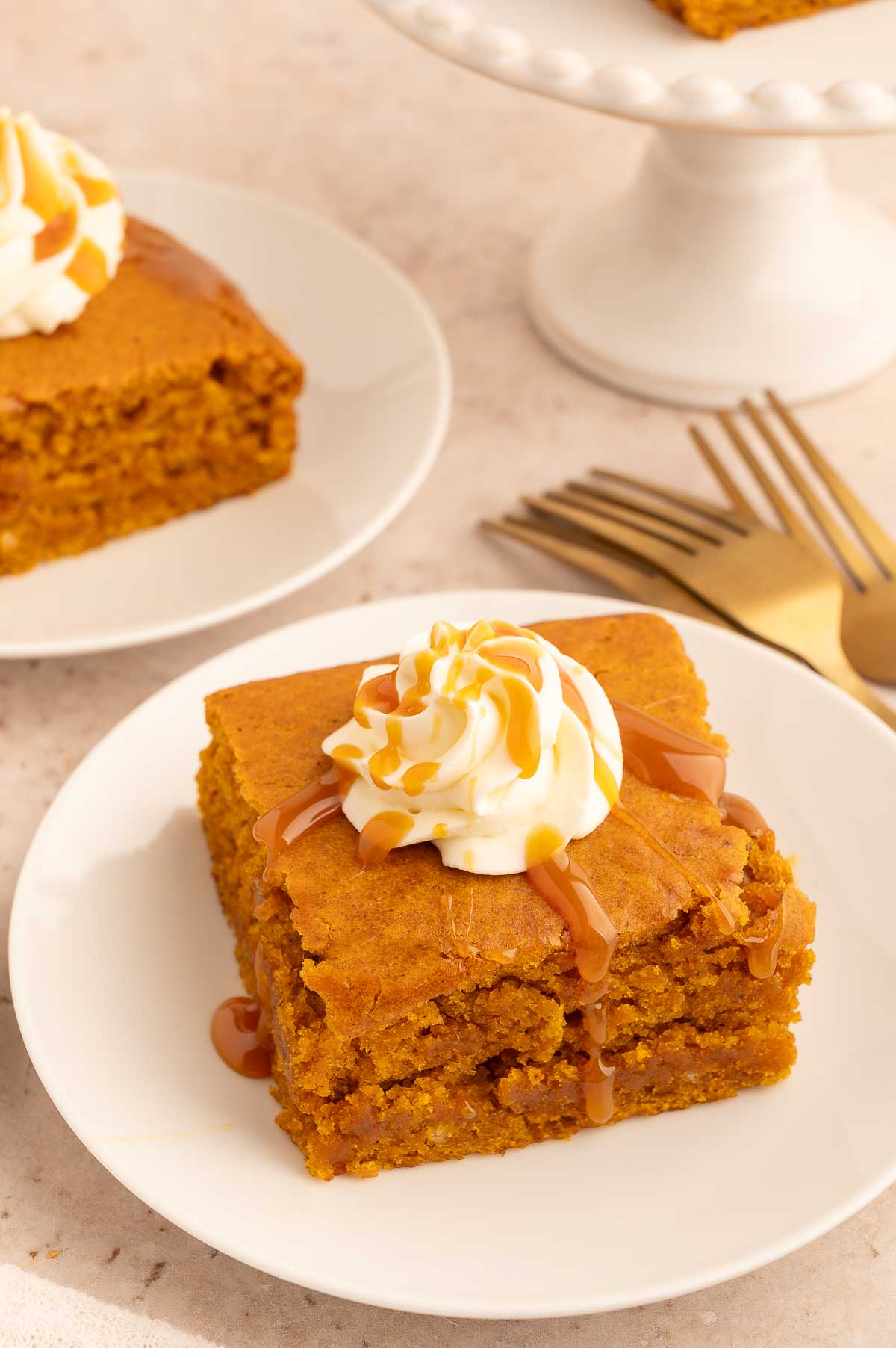 Delicious vegan pumpkin spice cake topped with whipped cream and caramel drizzle.