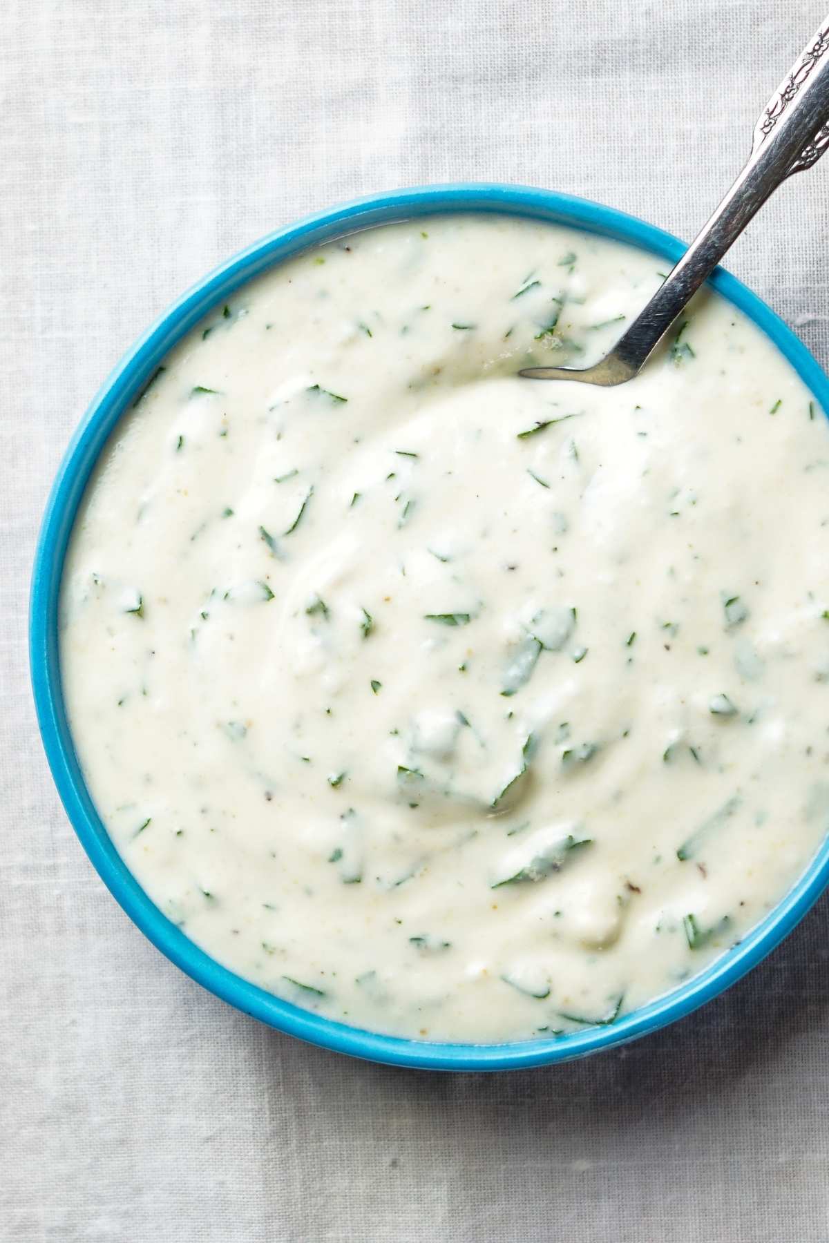 A bowl of vegan ranch dressing with specks of fresh green herbs.
