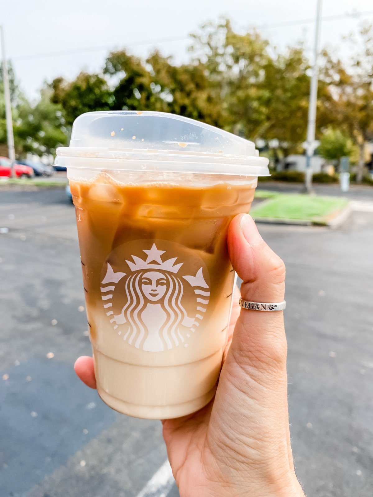 Woman with a vegan ring holding up a dairy-free Starbucks coffee drink that is brown on top and white on the bottom.