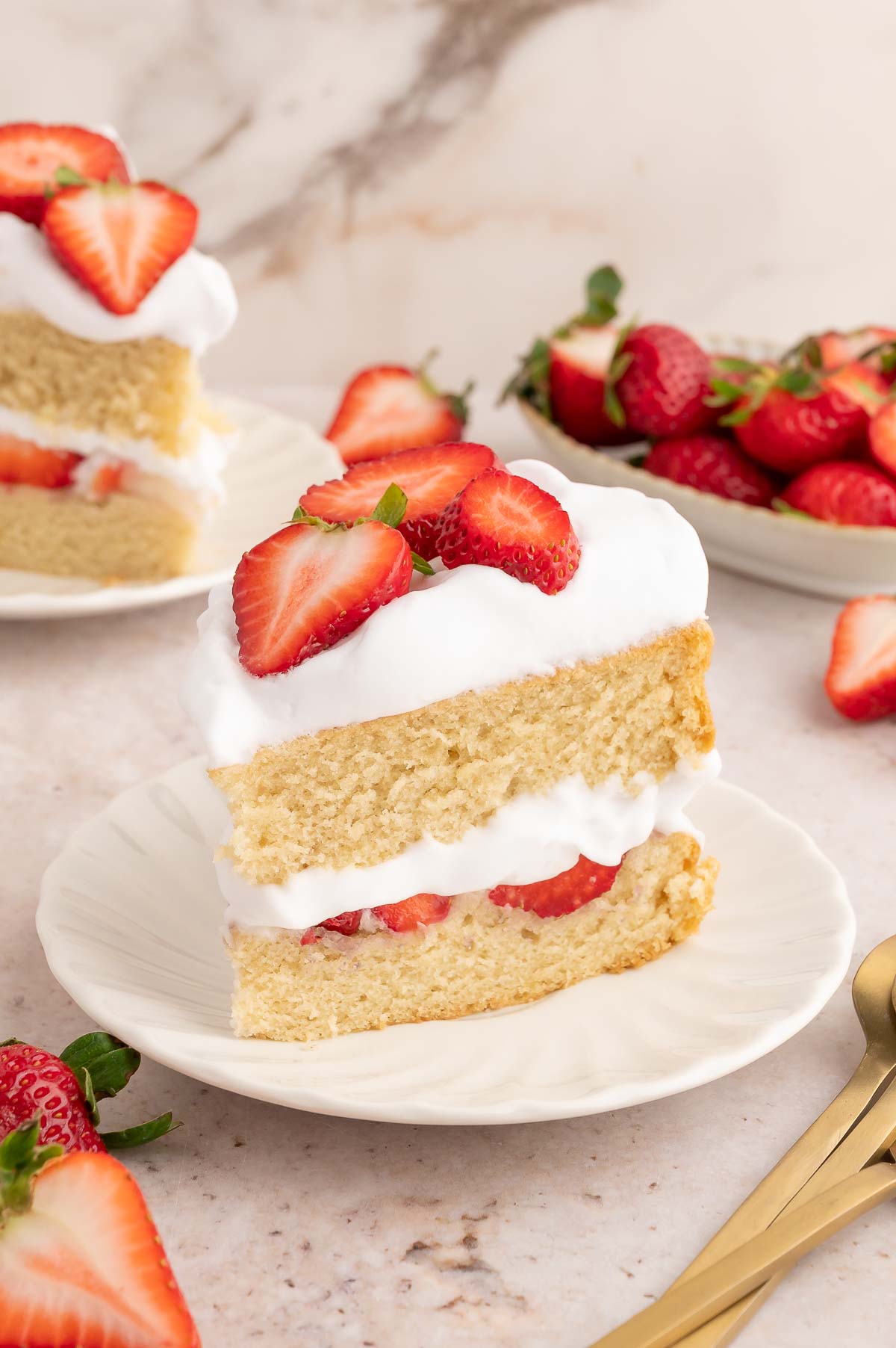 A slice of vegan strawberry shortcake cake topped with vegan whipped cream and sliced strawberries.