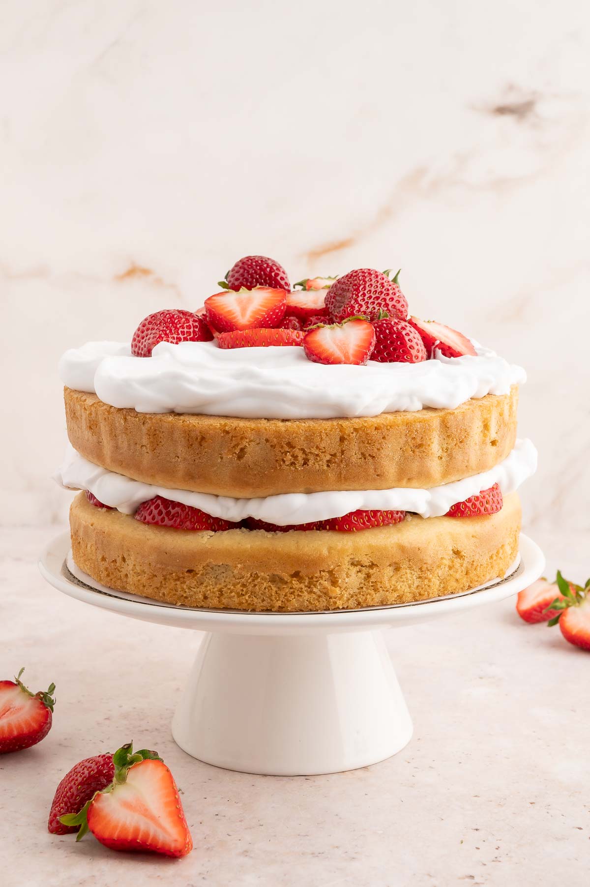 A 2-layer vegan strawberry shortcake cake topped with coconut whipped cream and sliced fresh strawberries.