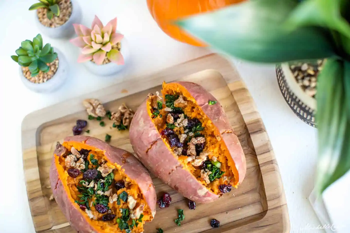 Stuffed Sweet Potatoes on a cutting board topped with dried cranberries and candied walnuts.