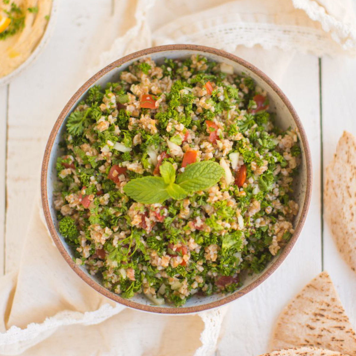 Vegan tabbouleh salad on a white wooden countertop garnished with mint and next to cut slices of pita bread.