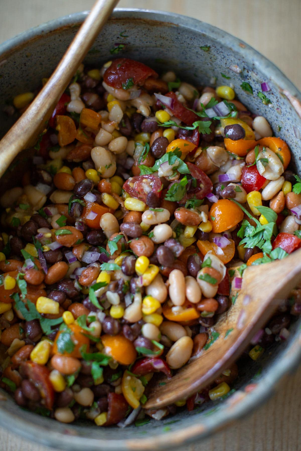 Vegan three bean salad with white beans, kidney beans, black beans, tomatoes, and cilantro in a large mixing bowl.