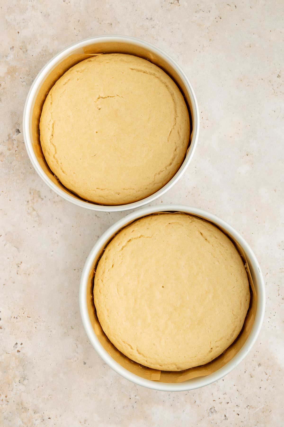 Two round pans of yellow vegan vanilla cake sitting on top of a white surface.