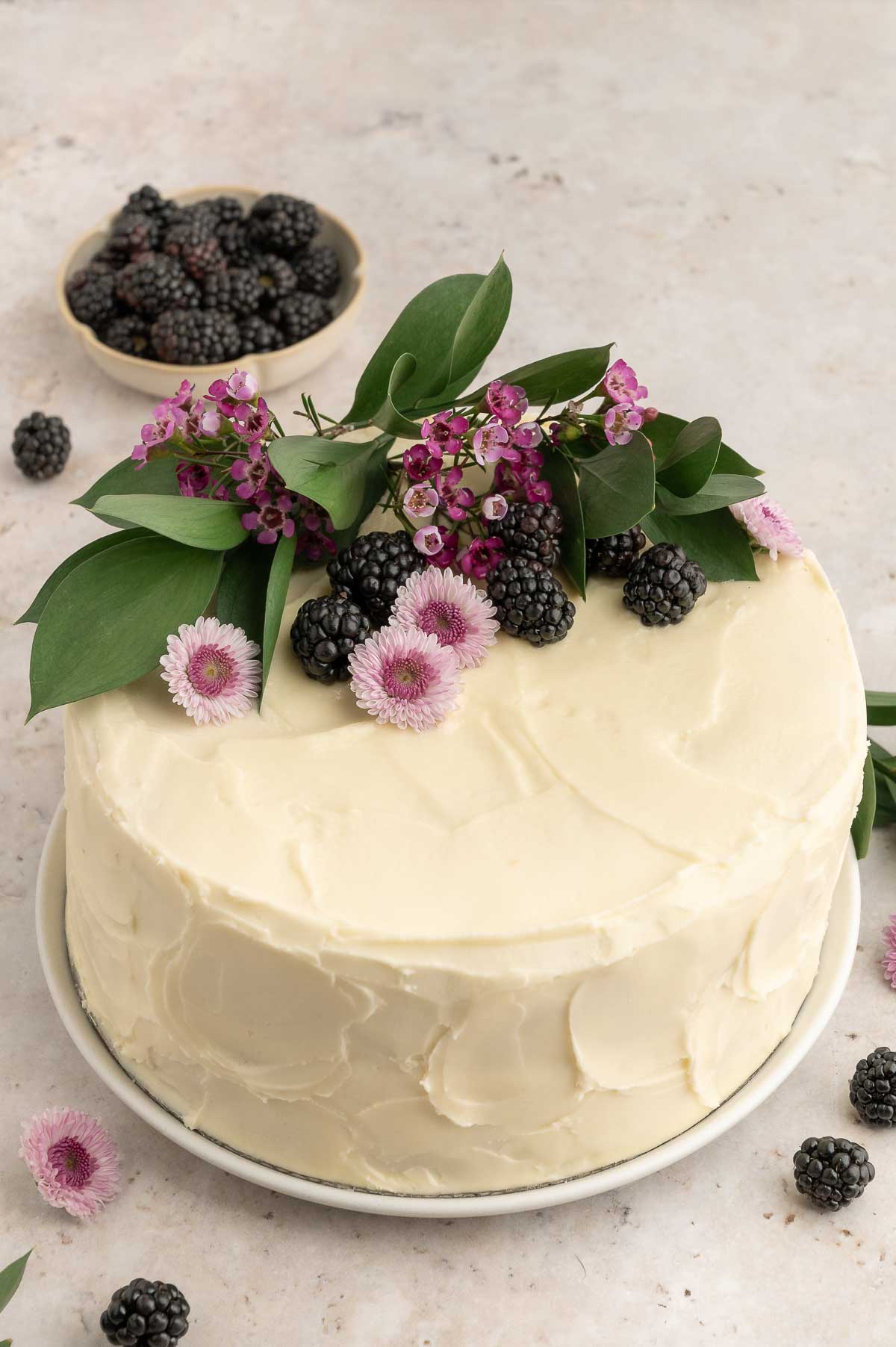 A vegan vanilla cake with white frosting and blackberries.